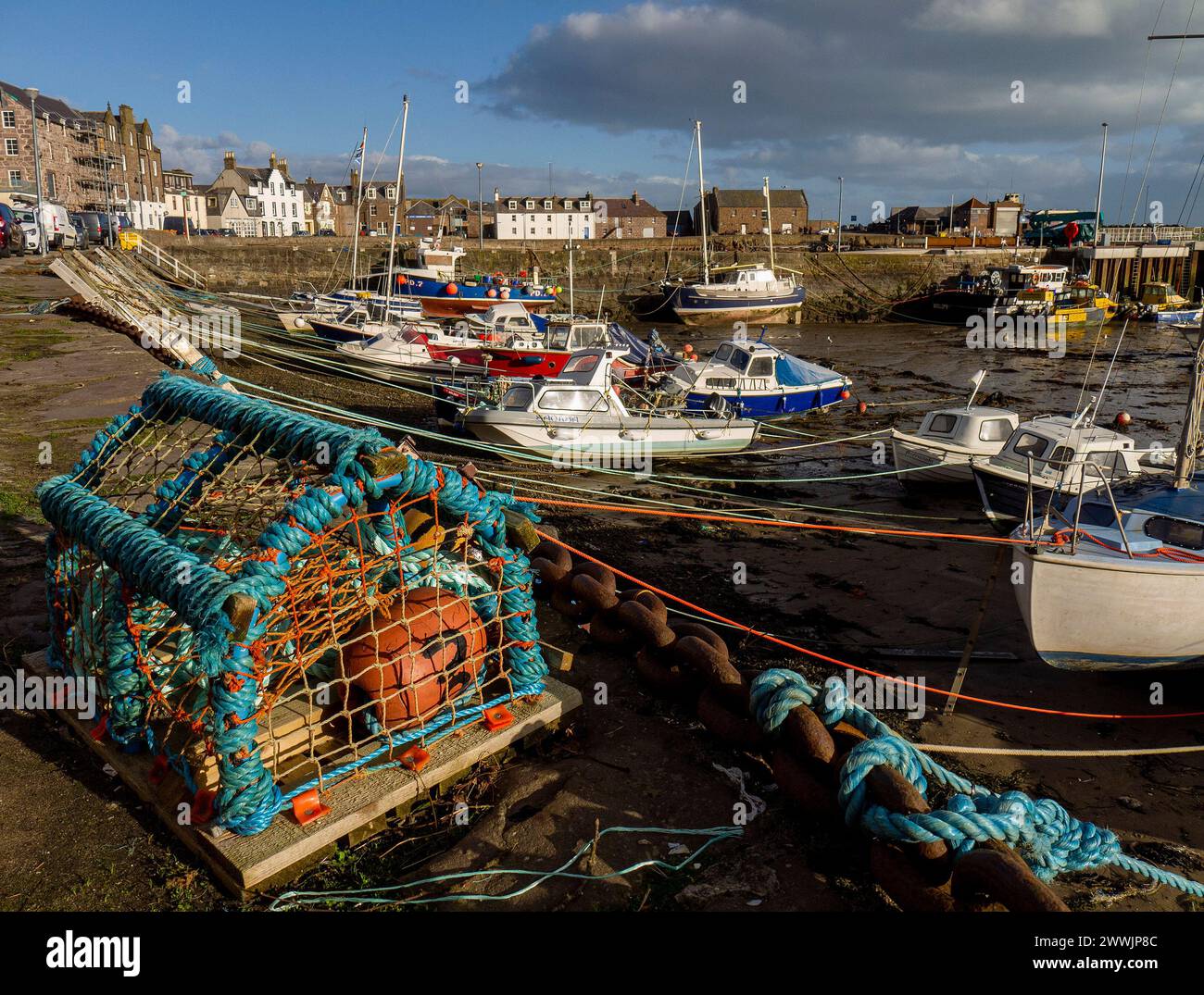 Ein Hummertopf und Fischerboote bei Ebbe in Cowie Harbour, Stonehaven Bay, Stonehaven, Aberdeenshire, Schottland, UK Stockfoto