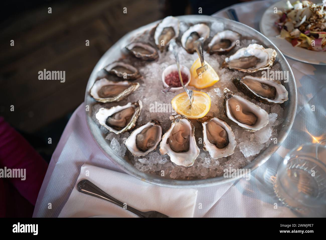 Steinaustern, zubereitet zum Teilen in einem großen Gericht, in ihrer Schale, serviert auf Eis mit Zitrone und Relish. Stockfoto