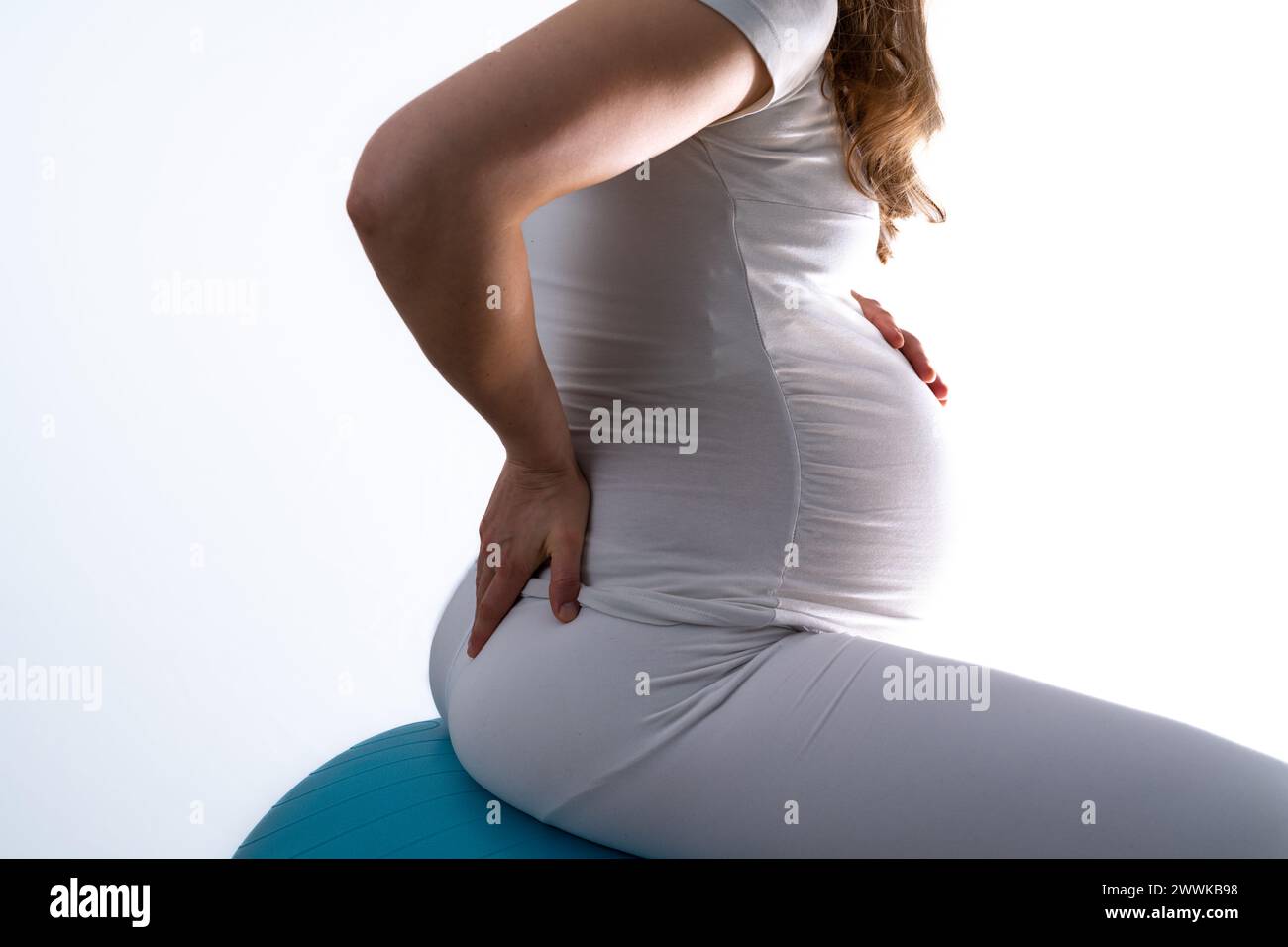 Beschreibung: Schwangere Frau mit Baby-Unebenheit auf Gymnastikball fühlt Rückenschmerzen und hält die Hand auf ihrem schmerzenden Rücken. Letzter Schwangerschaftsmonat - Woche 36. Si Stockfoto