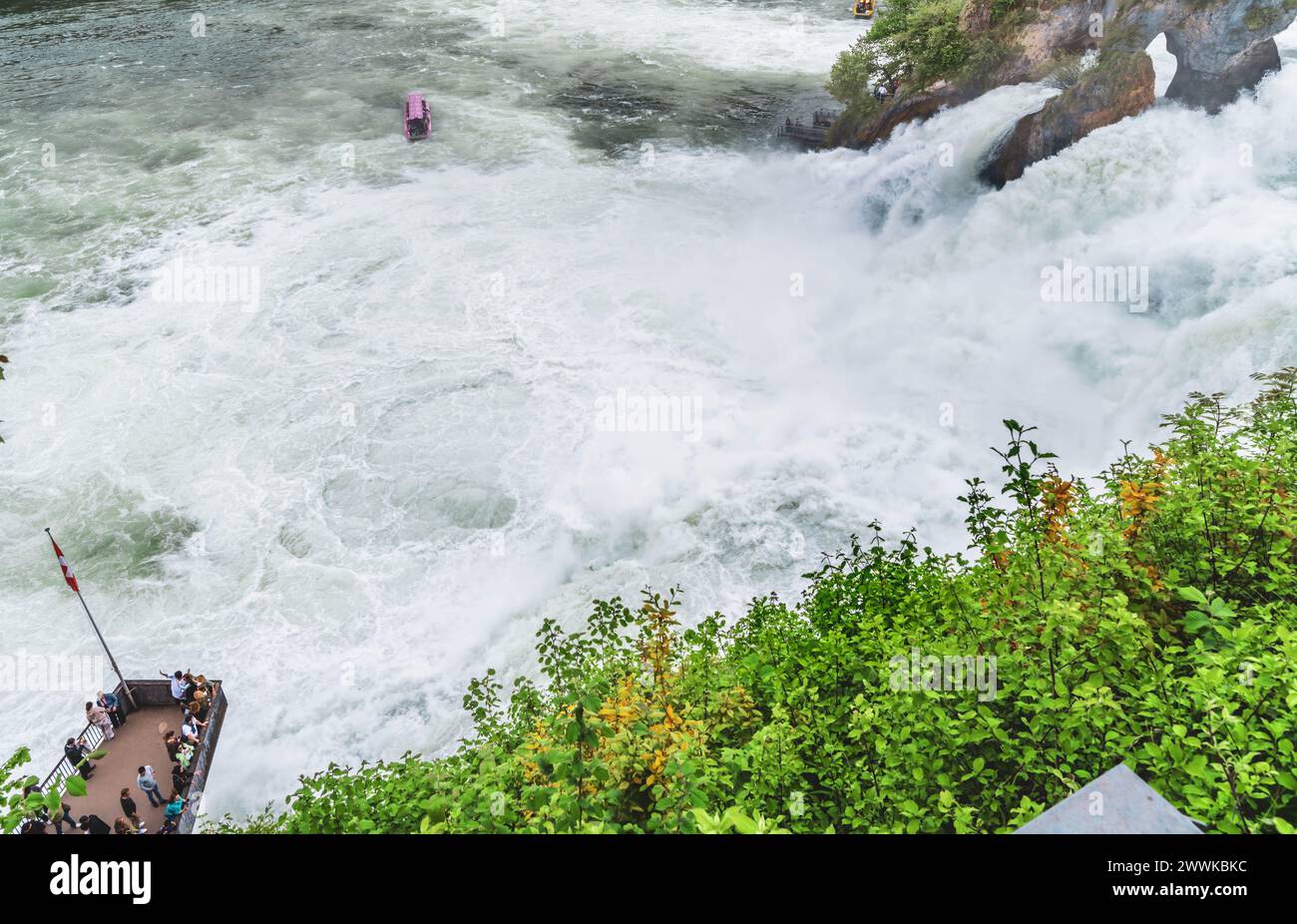 Beschreibung: Touristen beobachten die massiven Wasserfälle unter Schloss Laufen am Rheinfall von der Plattform und dem Touristenboot aus. Rheinfall, Neuhausen A Stockfoto