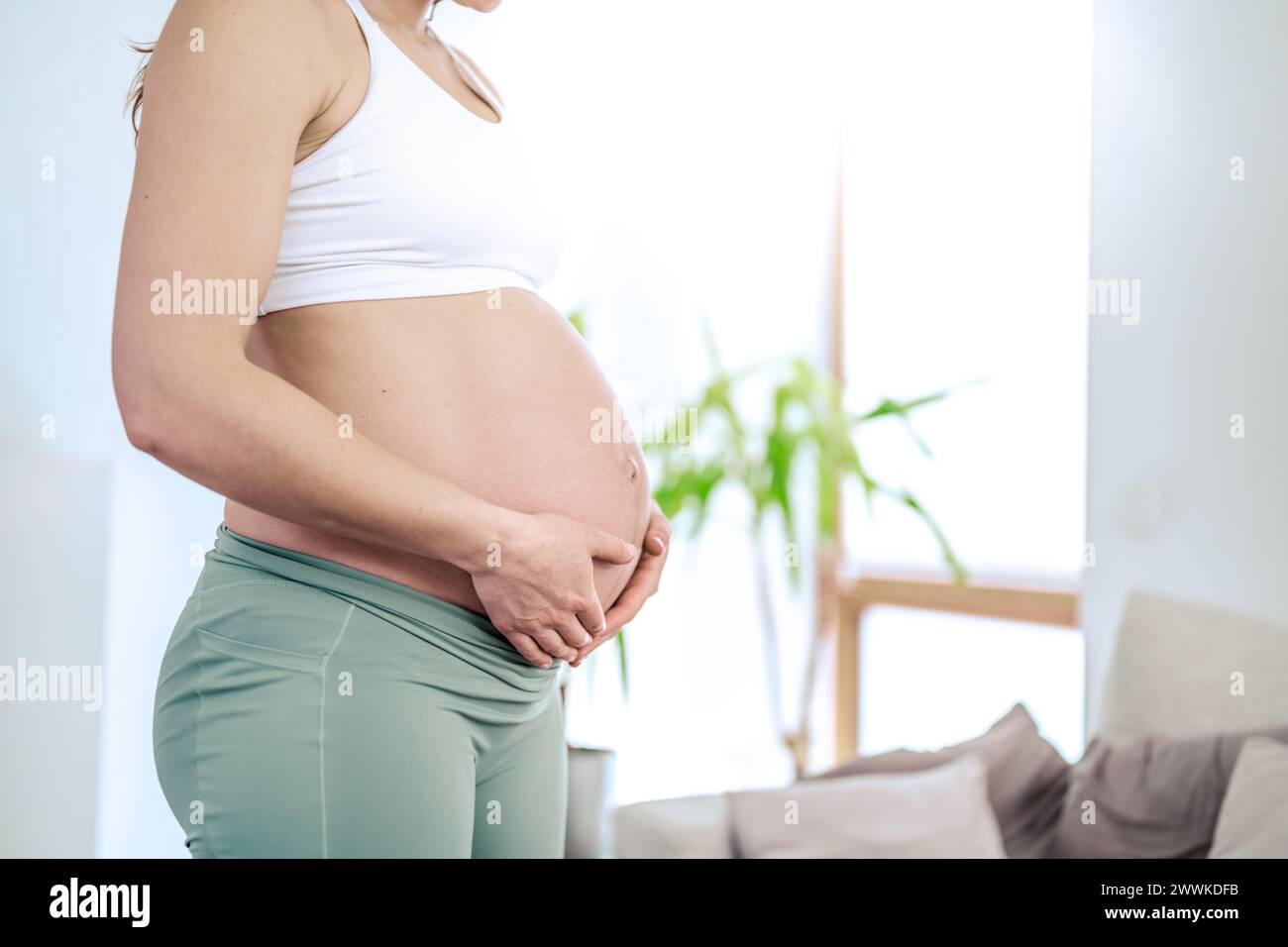 Beschreibung: Laterale Ansicht des Mittelschnitts einer nicht erkennbaren Frau, die ihren Bauch in den letzten Schwangerschaftsmonaten sanft hält. Schwangerschaft erstes Trimenon - Wee Stockfoto