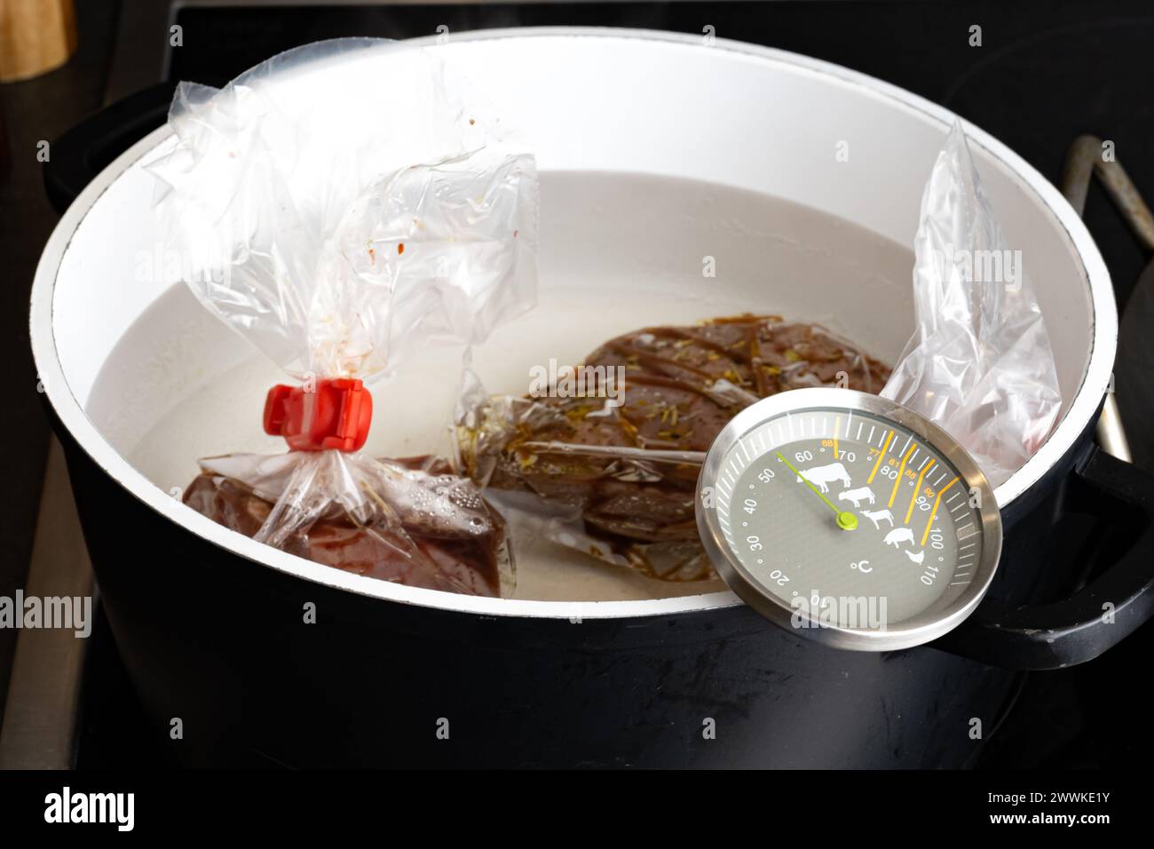 Beschreibung: Zubereitung von rohem Rinderfiletsteak für ein Sous-Vide-Bad in einem Topf mit Thermometer auf dem Küchenherd, von der Seite fotografiert. Stockfoto