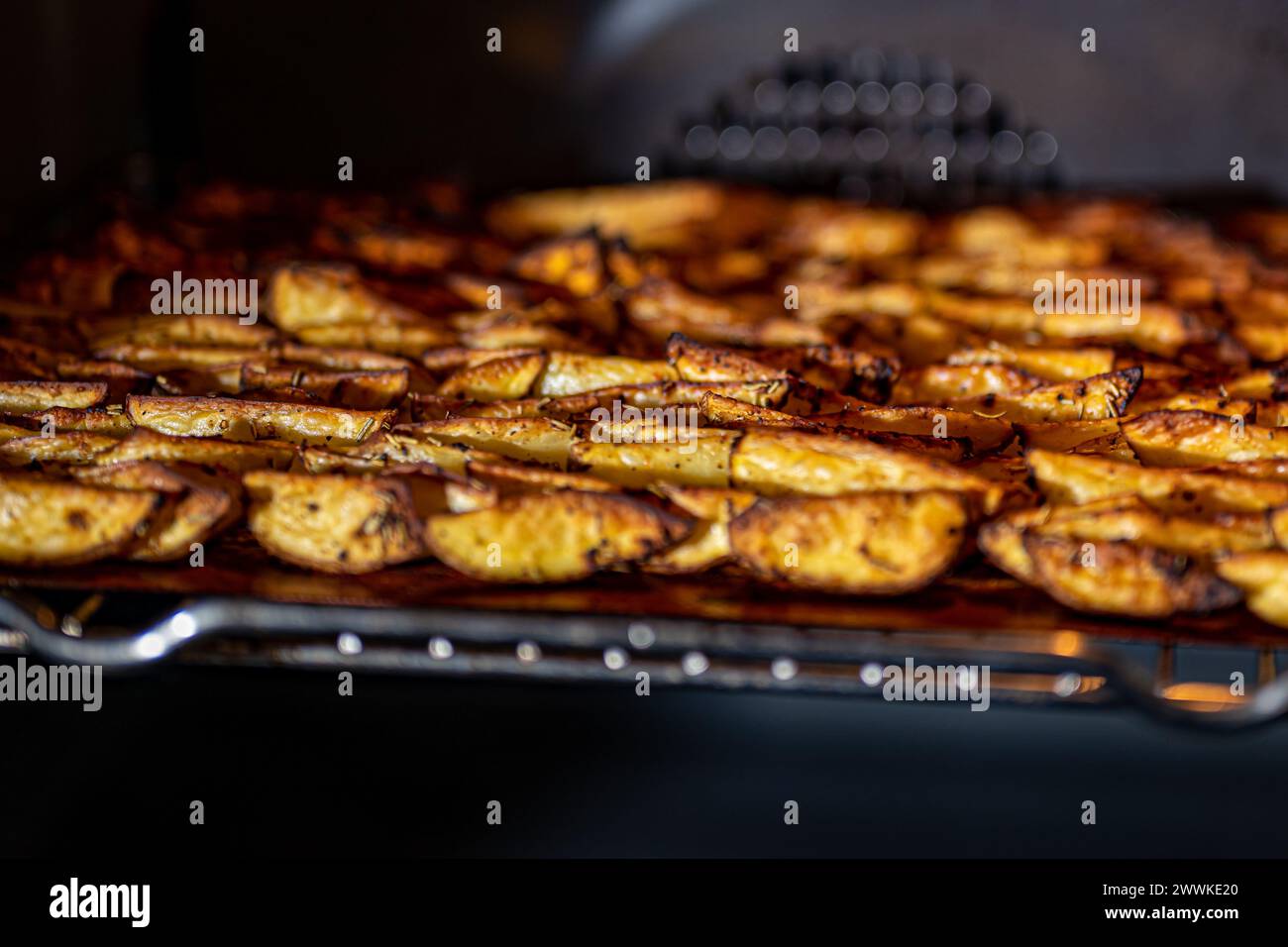 Beschreibung: Knusprige, goldbraune, gebackene Kartoffelkeile mit Paprika, Knoblauch, Salz, Pfeffer, Rosmarin, basilikum auf dem Tablett im Ofen, fotografiert von Stockfoto