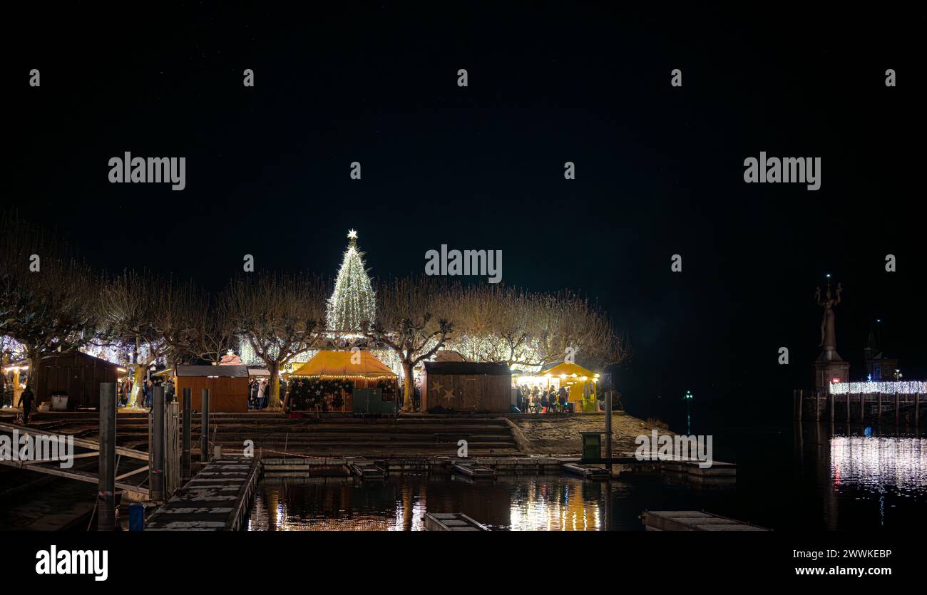 Beschreibung: Besucher des Weihnachtsmarktes mit wunderschön dekoriertem Glühweinstand genießen die Winteratmosphäre mit Schnee auf den Bäumen. Konstanz (Kon Stockfoto