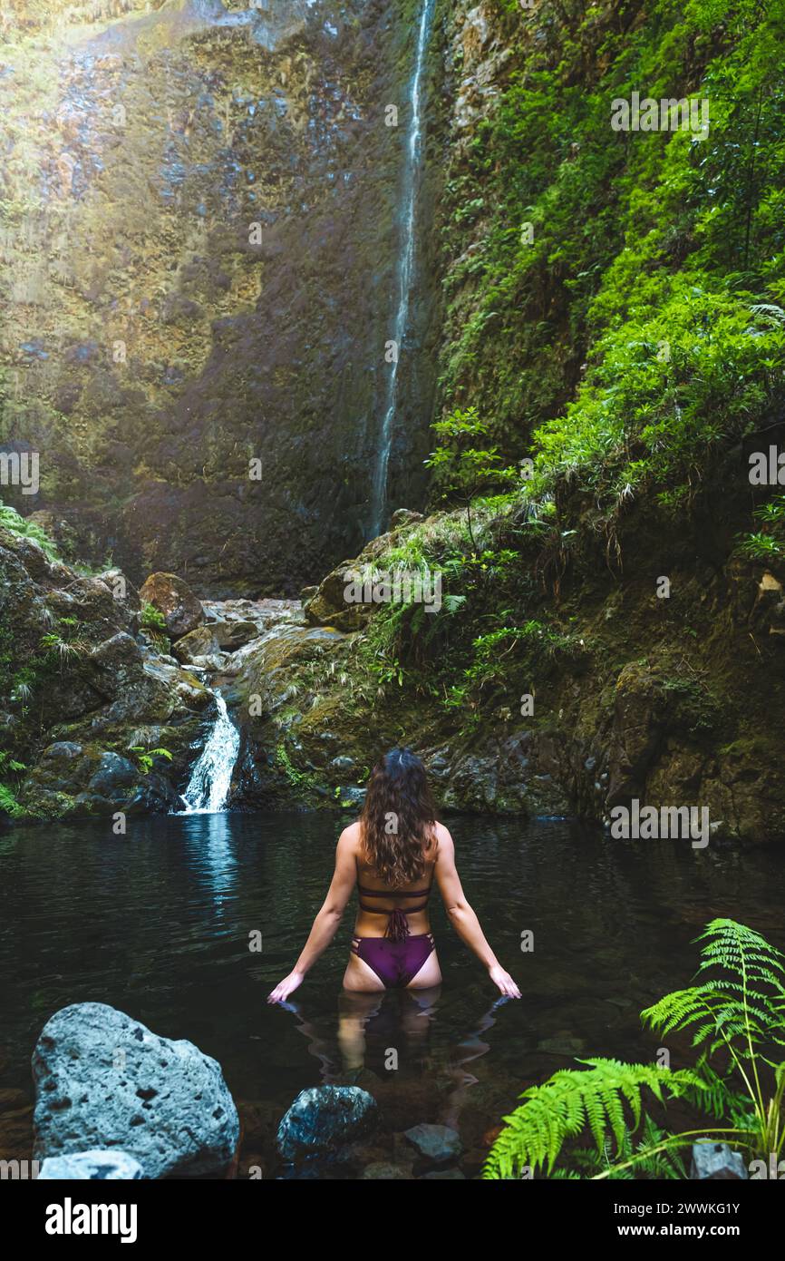Beschreibung: Touristenfrau im Bikini genießt ein erfrischendes Bad im Pool an einem malerischen überwucherten Wasserfall im Madeira Regenwald. Levada von Caldei Stockfoto