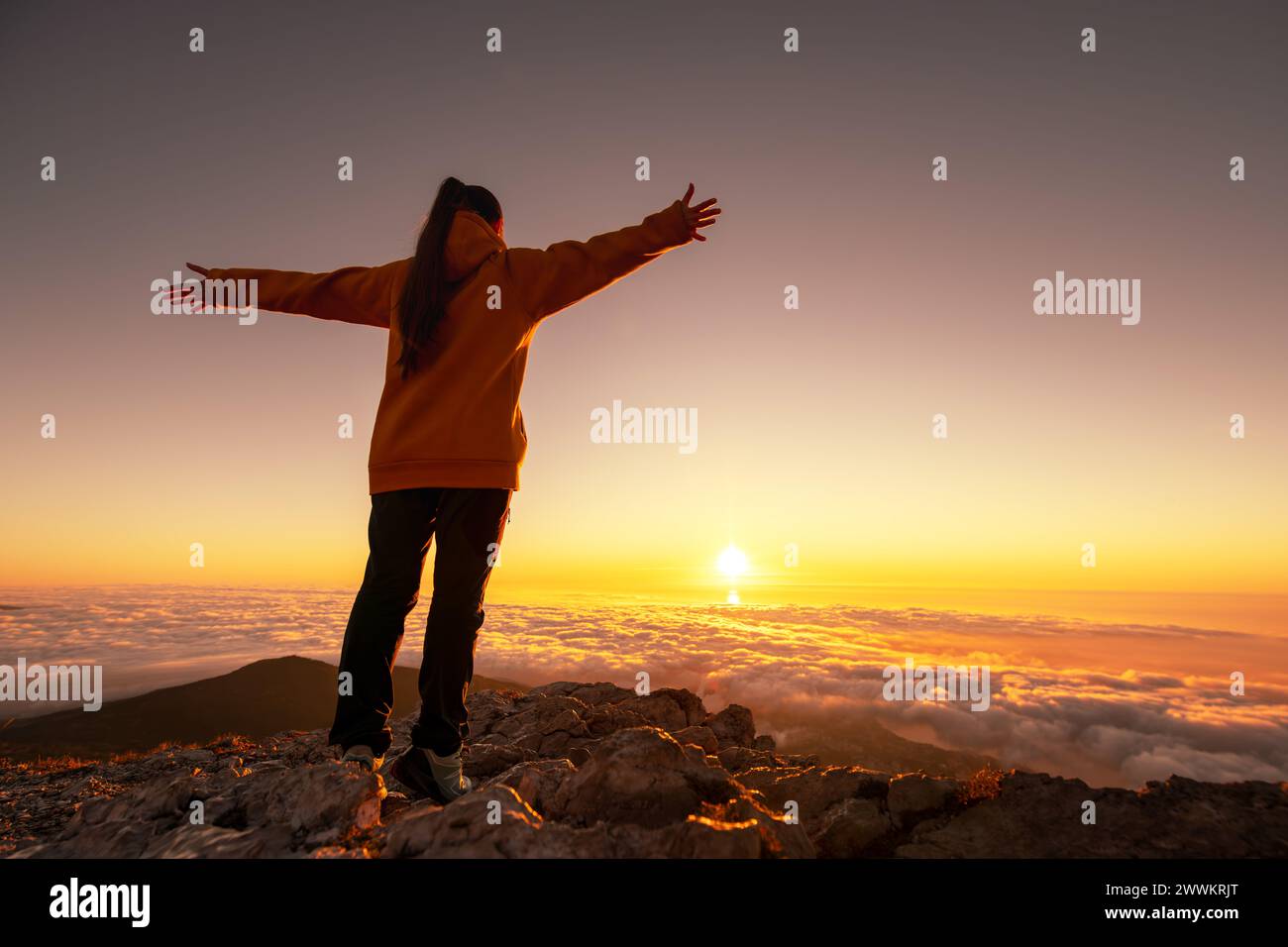 Glücklicher Wanderer oder Tourist ohne Rucksack steht mit offenen Armen auf der Bergspitze und genießt den Sonnenaufgang Stockfoto