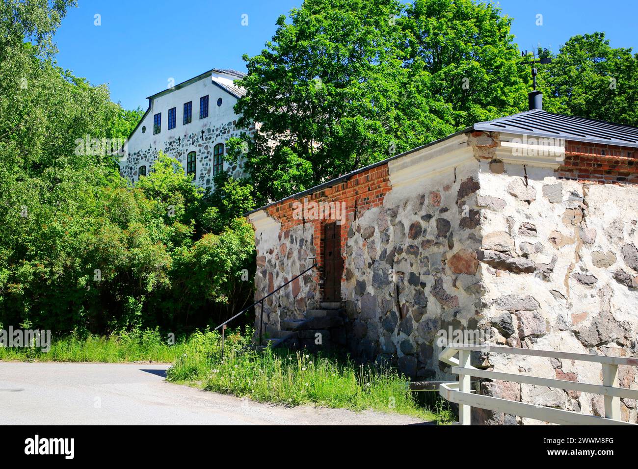 Sjundby Manor. Die mittelalterliche Steinburg aus den 1560er Jahren auf dem Hintergrund, Steinspeicher auf der rechten Seite. Siuntio, Finnland. Mittsommer, 24. Juni 2022. Stockfoto