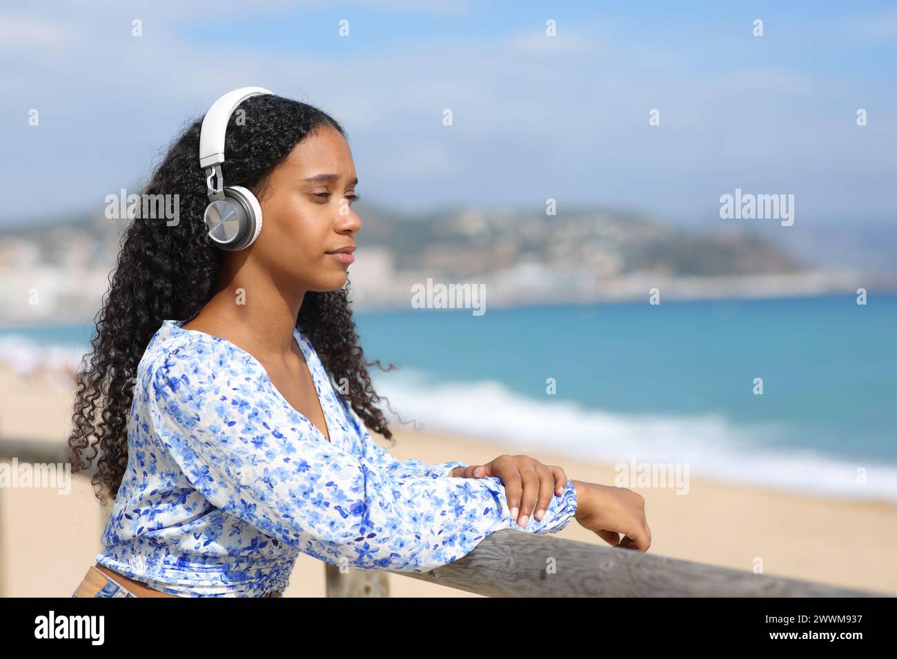 Eine ernste schwarze Frau, die am Strand Audio hört und wegblickt Stockfoto