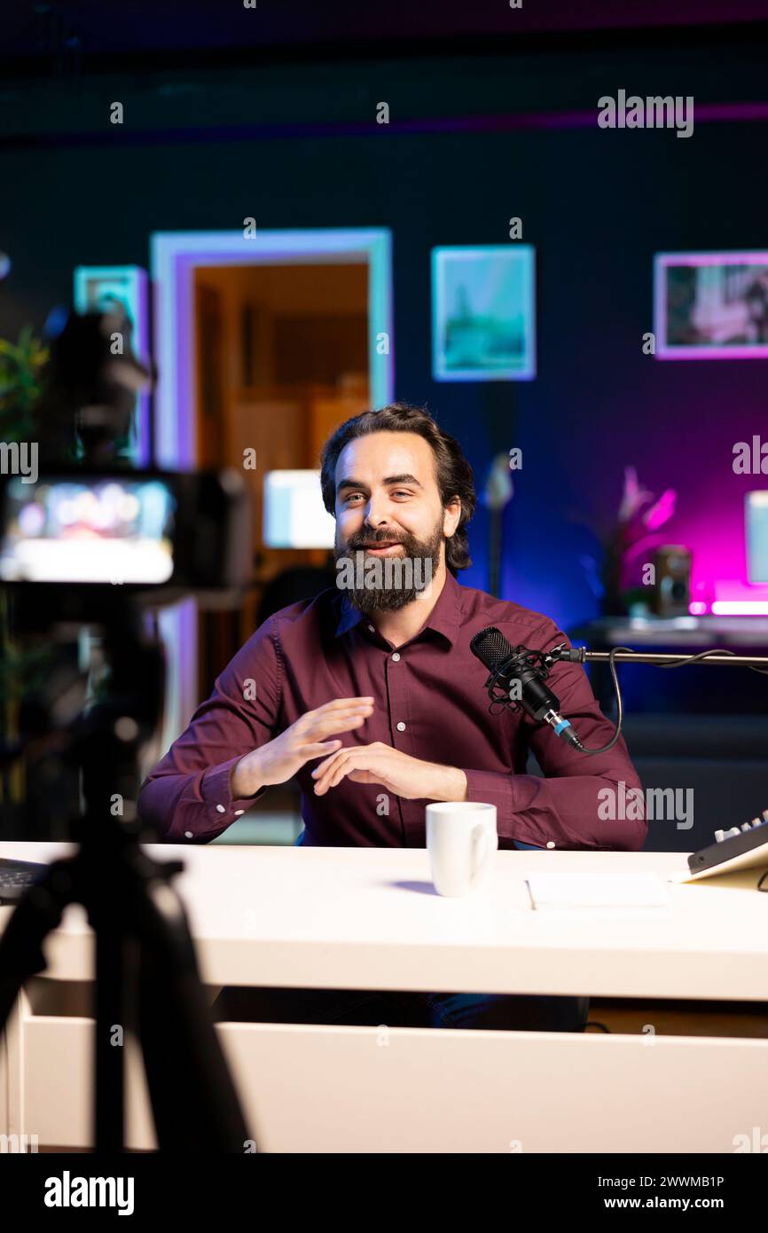Fröhlicher Internet-Star, der sich vor der professionellen Kamera und dem hochwertigen Mikrofon im Studio unterhalten und mit den Zuschauern diskutiert. Fröhlicher Mann, der High-Tech-Aufnahmegeräte benutzt, um Social-Media-Videos aufzunehmen Stockfoto