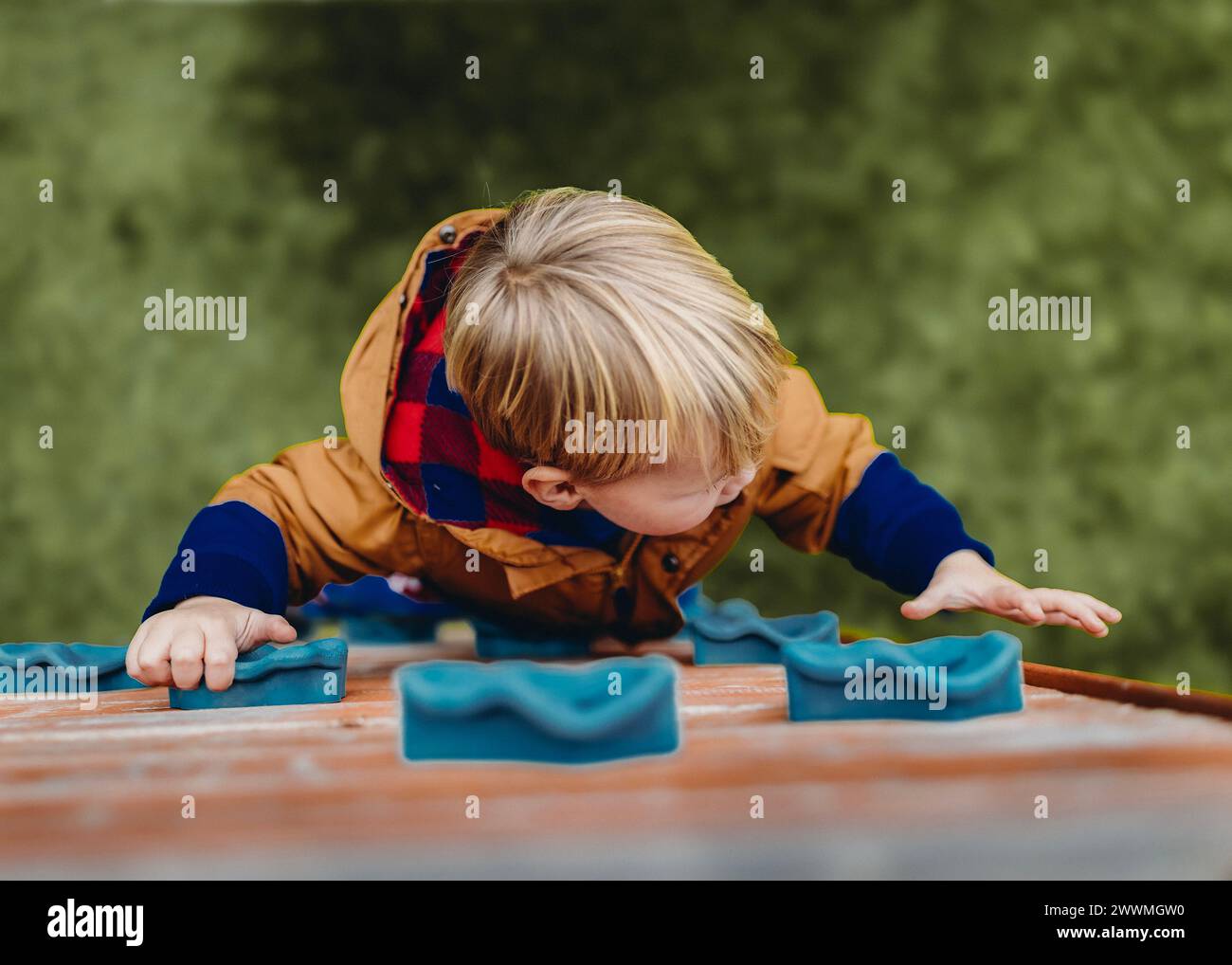 Abenteuerlustige, blonde Kleinkinder erobert den Spielplatz an der Kletterwand. Stockfoto