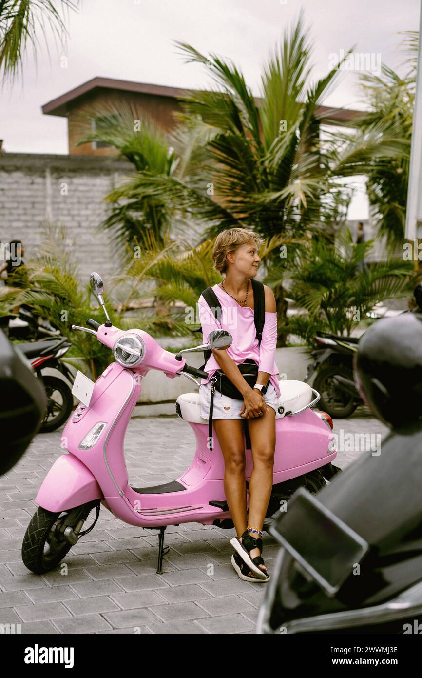 Eine junge Frau mit kurzen Haaren auf einem pinkfarbenen Vespa-Roller. Stockfoto