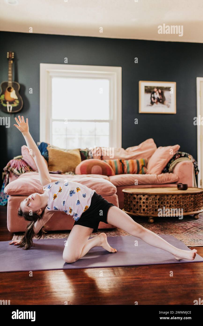 Das junge Mädchen macht eine Seitenplanke auf der lila Yogamatte im Wohnzimmer Stockfoto