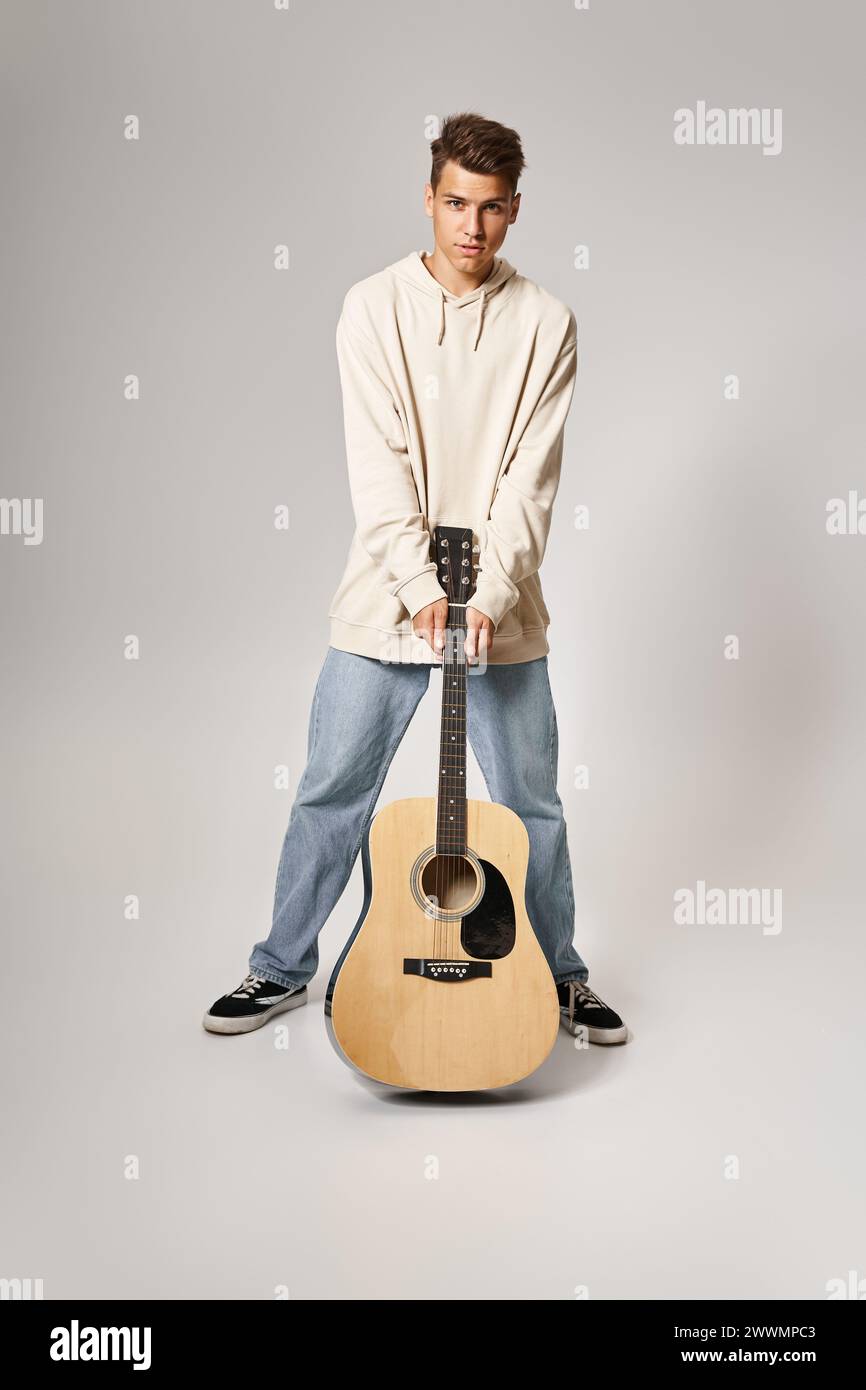 Charismatischer Mann im lässigen Outfit mit braunen Haaren, der mit Gitarre auf hellem Hintergrund steht Stockfoto