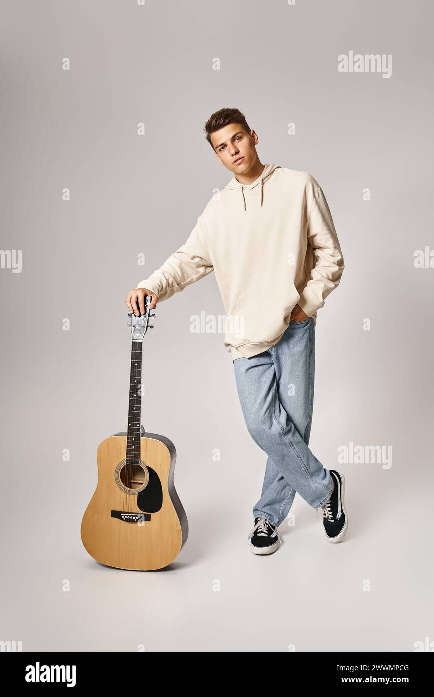 Charismatischer junger Mann in lässigem Outfit mit braunen Haaren, die auf der Gitarre vor hellem Hintergrund liegen Stockfoto