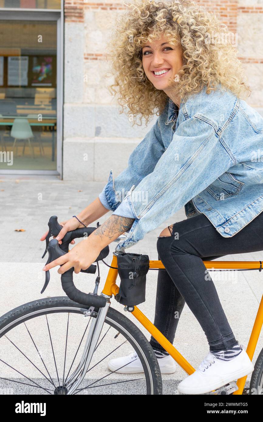 Junge weiße Frau mit lockigen blonden Haaren, lächelnd, auf einem klassischen gelben Fahrrad Stockfoto