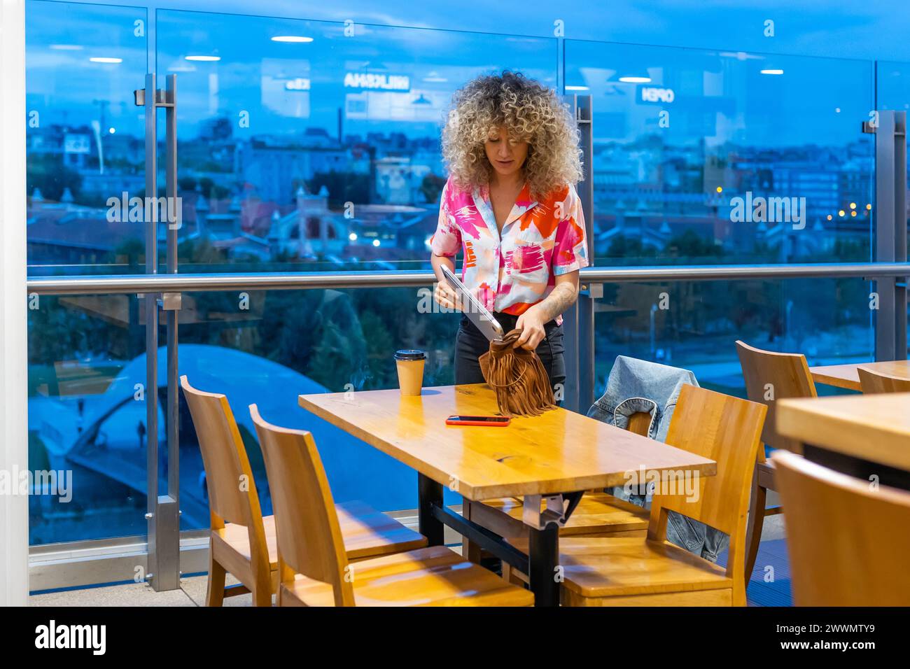 Porträt einer lächelnden jungen kaukasischen Frau mit lockigen blonden Haaren, die in einem Café mit Laptop und Smartphone arbeitet, aufnimmt und geht Stockfoto