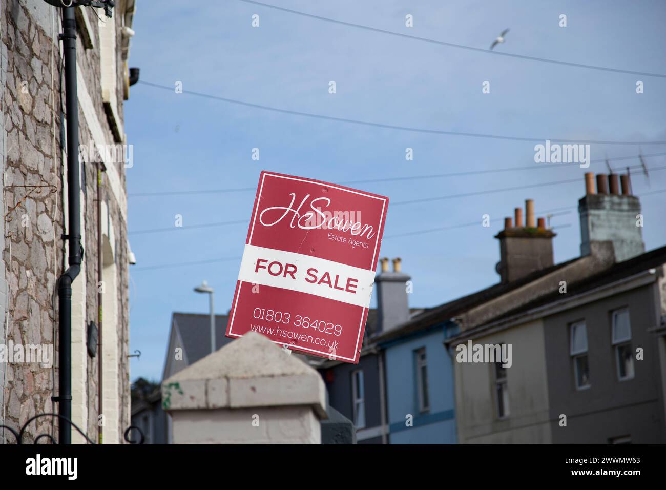 H Sowen Immobilienmakler rot-weiß zum Verkauf Schild vor der Straße mit Reihenhäusern vor blauem Himmel Stockfoto