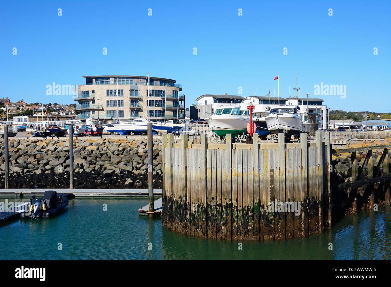 Boote im Trockendock im Hafen mit dem Ellipse-Gebäude hinten, West Bay, Dorset, Großbritannien, Europa. Stockfoto