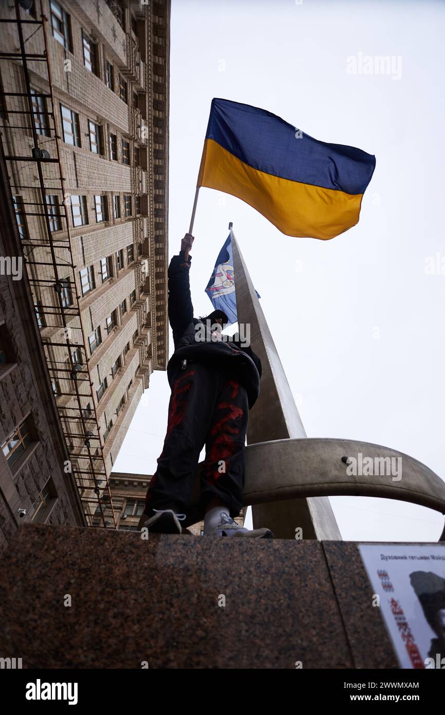 Ukrainischer Patriot, der mit Nationalflagge auf einem Denkmal winkt. Kiew - 23. März 2024 Stockfoto