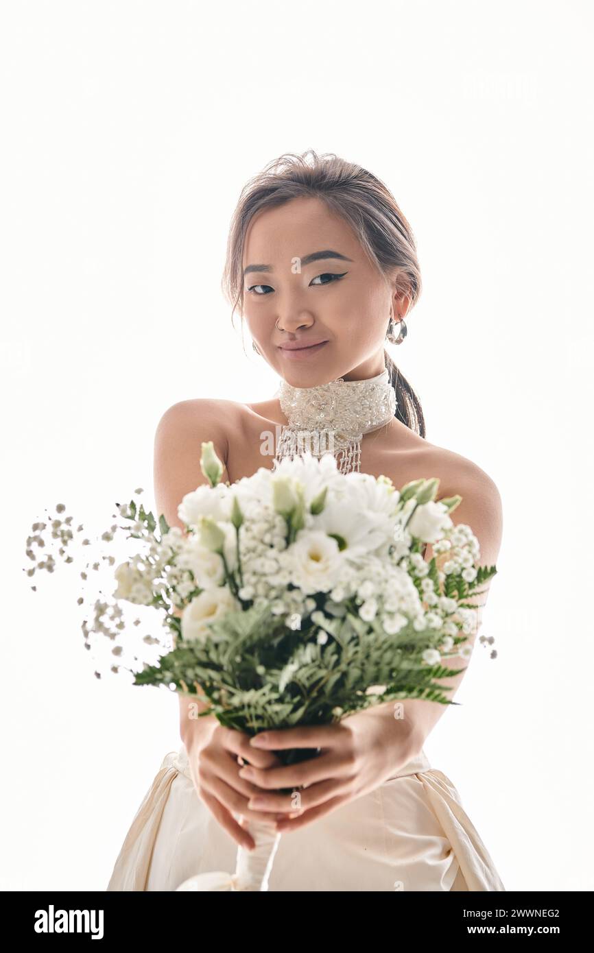 Attraktive junge asiatische Frau mit Gnade Make-up halten Strauß von weißen Blumen auf hellem Hintergrund Stockfoto