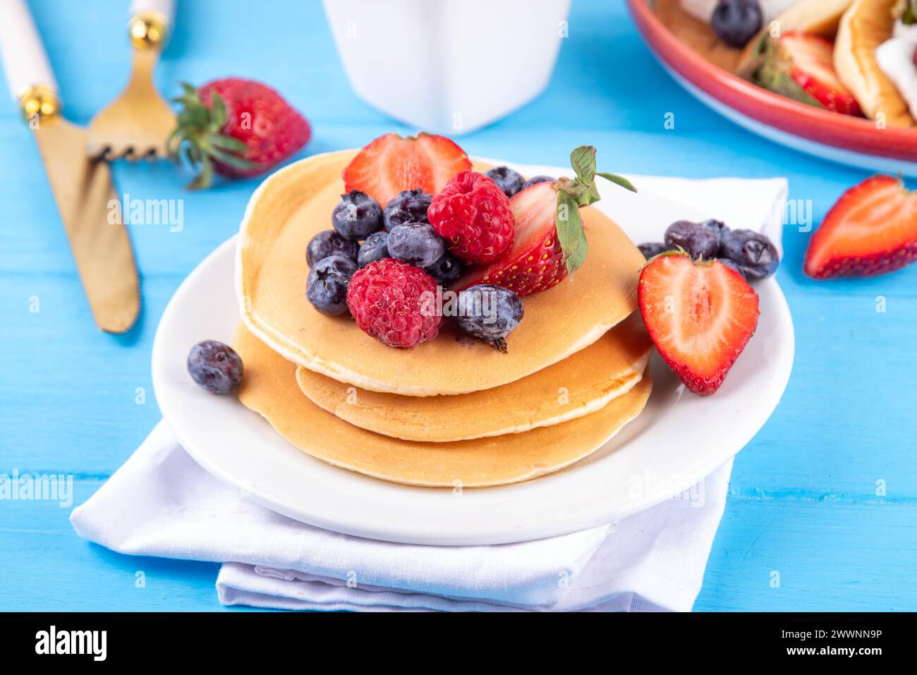 Stapel traditioneller amerikanischer Pfannkuchen mit Sommerbeeren. Frühstück süße Pfannkuchen mit Honig, Erdbeere und Heidelbeere, am Morgen sonnenblau Stockfoto