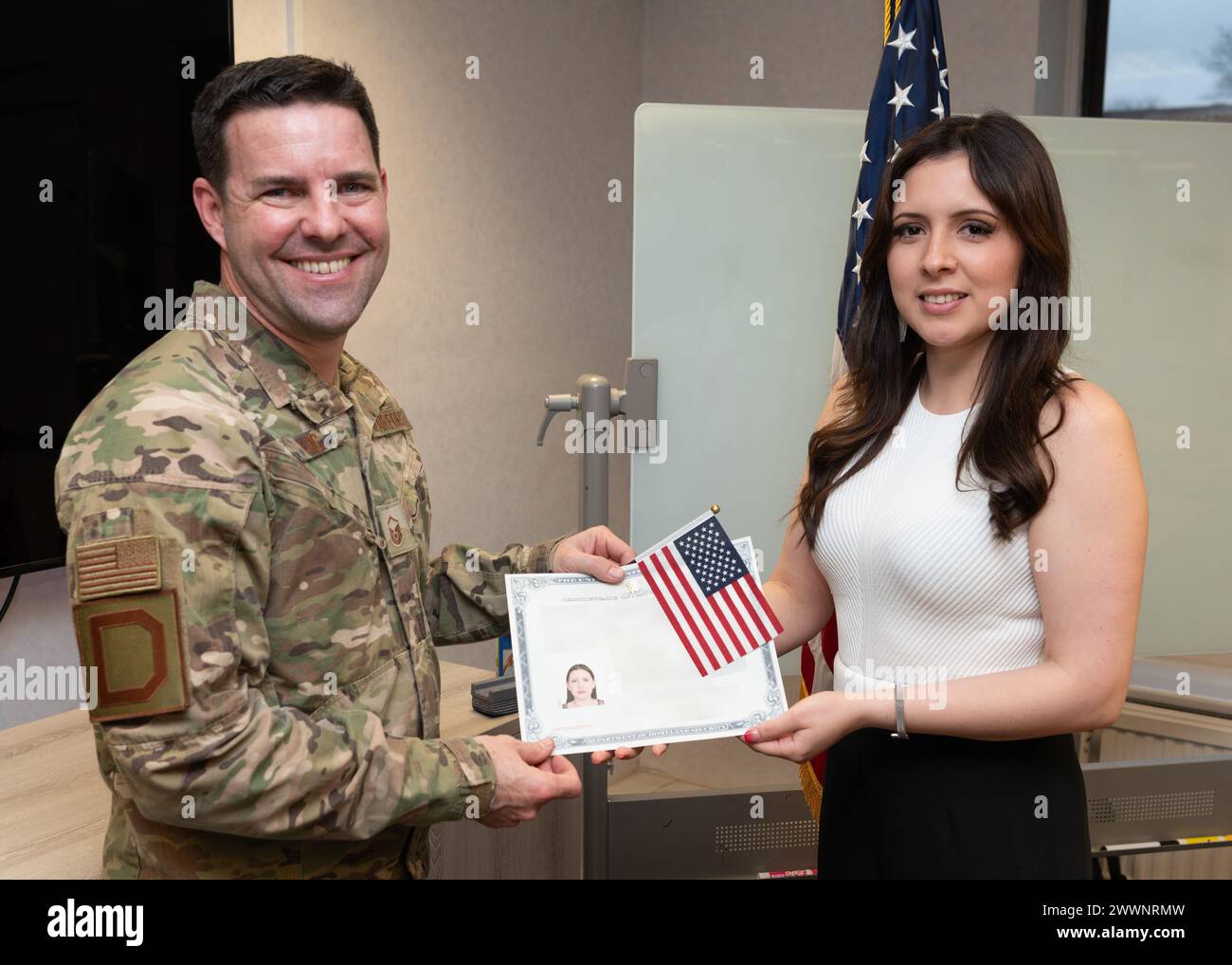 Chris King, Leiter des Military & Family Readiness Center, unteroffizieller Offizier des U.S. Air Force Master Sgt., überreicht Maria Kozain ihr Einbürgerungszertifikat in den USA bei der Royal Air Force Mildenhall, England, 13. Februar 2024. Kozain war eine Staatsbürgerin von Honduras, bevor sie als Staatsbürgerin der USA wurde. Luftwaffe Stockfoto