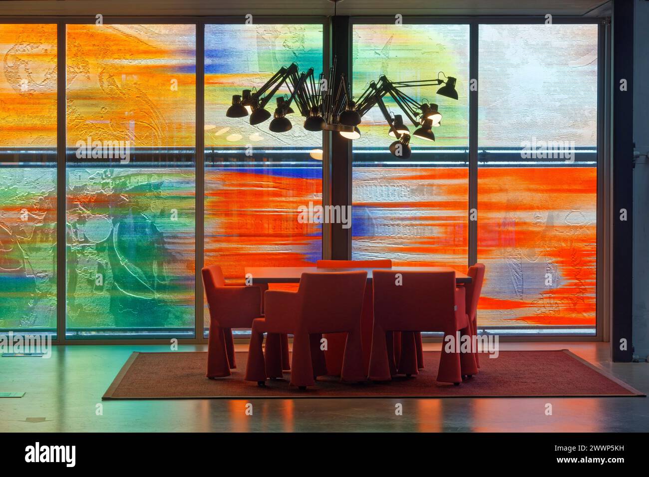 Tisch und Stühle im Bürobereich, vor mehrfarbiger Glasfassade, mit Reflexion auf dem Boden und Deckenlampe im Spinnenstil. Niederländisches Institut Für Sound Stockfoto