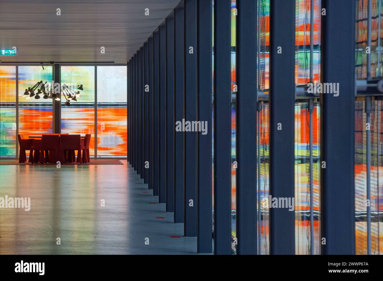 Tisch und Stühle im Bürobereich, vor mehrfarbiger Glasfassade, mit Reflexion auf dem Boden und Deckenlampe im Spinnenstil. Niederländisches Institut Für Sound Stockfoto