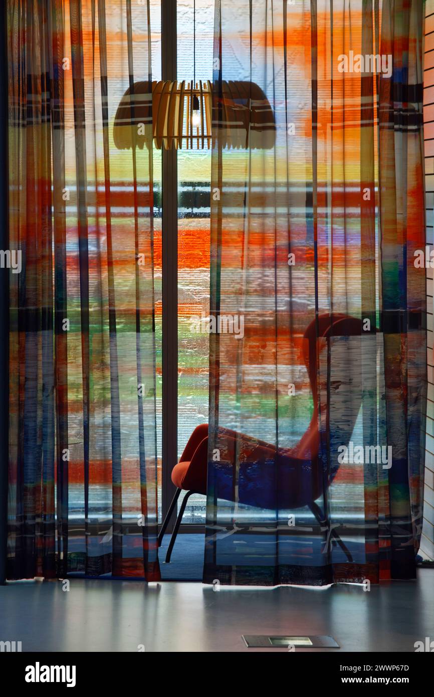 Stuhl im Bürobereich, mit Voile und Lampe vor mehrfarbiger Glasfassade. Dutch Institute For Sound & Vision, Hilversum, Niederlande. Architekt: N Stockfoto