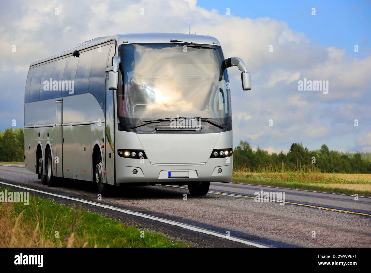 Silberner Reisebus, der im Spätsommer auf der Autobahn durch ländliche Landschaften fährt, blauer Himmel und Wolken im Hintergrund. Stockfoto