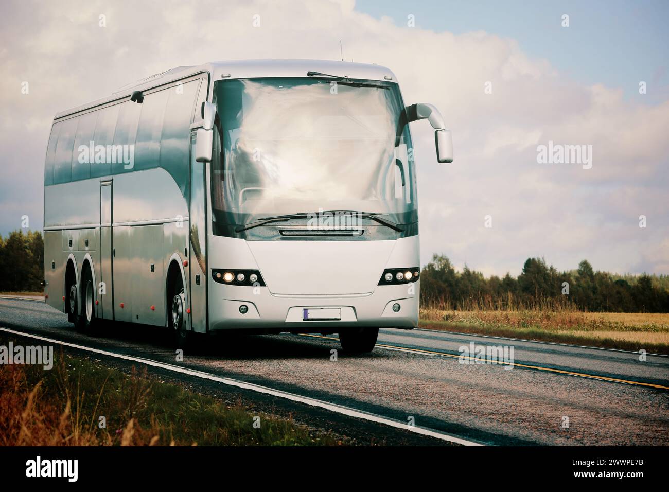 Silberner Reisebus, der auf der Autobahn durch ländliche Landschaften im herbstlichen Licht fährt. Stockfoto
