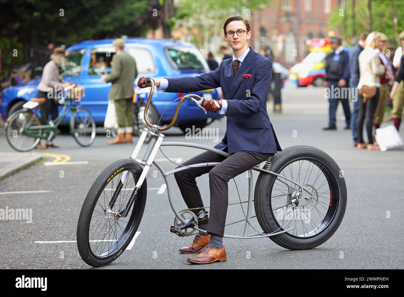 Ein junger Mann, der eine Suite und Krawatte trägt, fährt auf der Stadtstraße mit dem Low-Rider-Fahrrad. Stockfoto