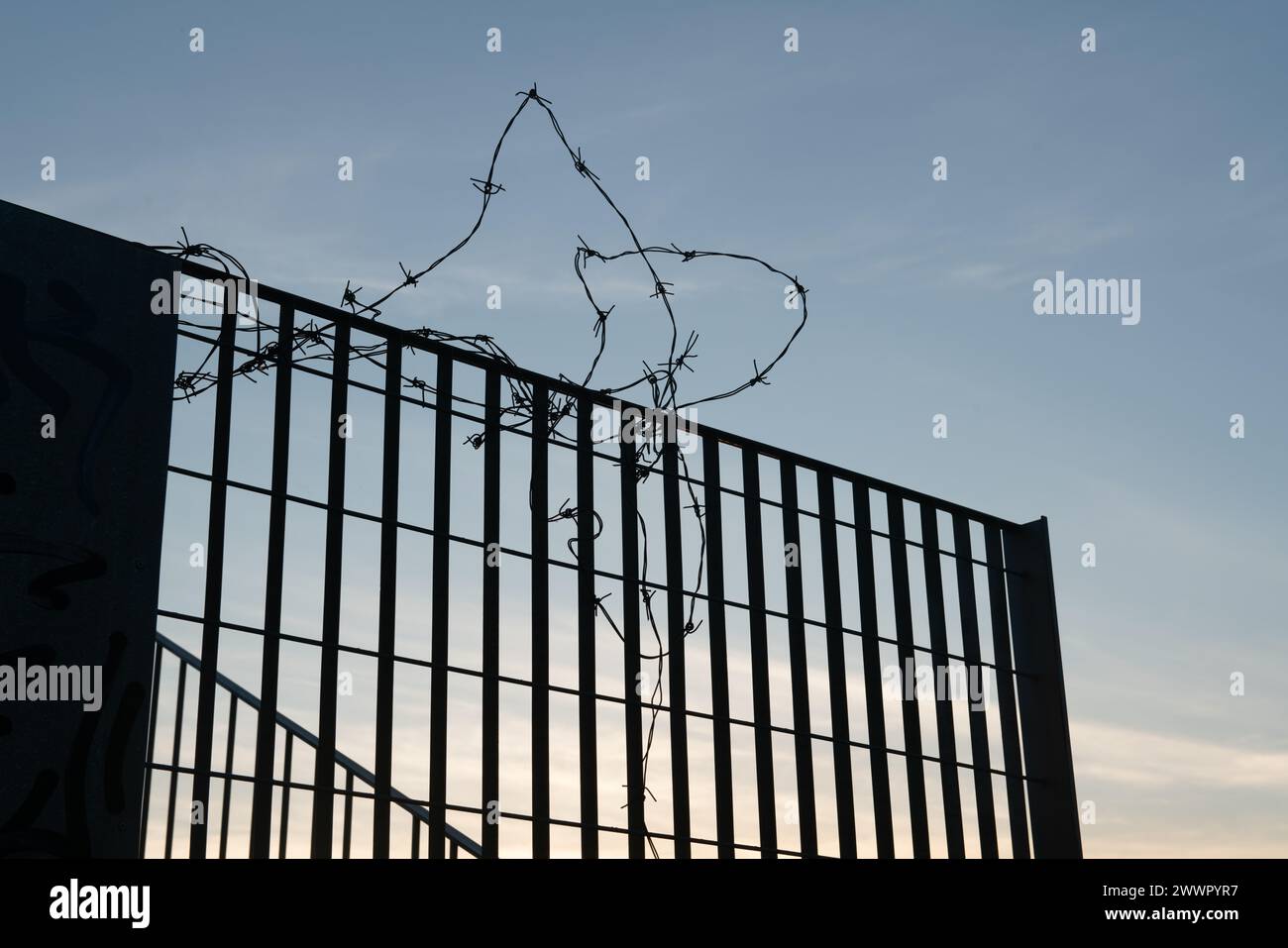 Silhouette eines Zauns mit Stacheldraht gegen das Licht, Symbol der Grenzen, Schließungen, Inhaftierungen, Inhaftierungen, und dramatische Momente im Histo Stockfoto