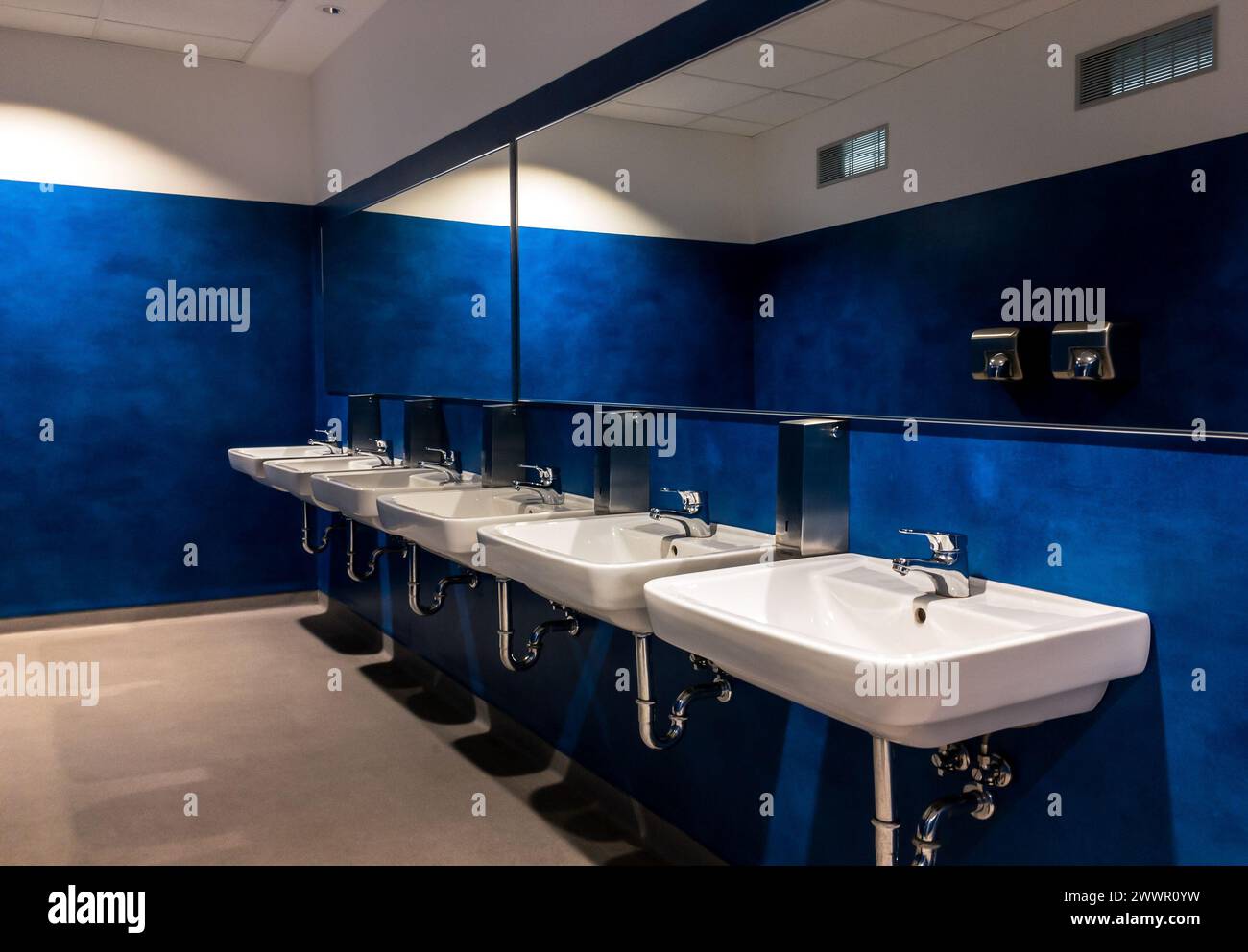 Sechs Waschbecken in einer modernen blauen Toilette mit großen Spiegeln Stockfoto