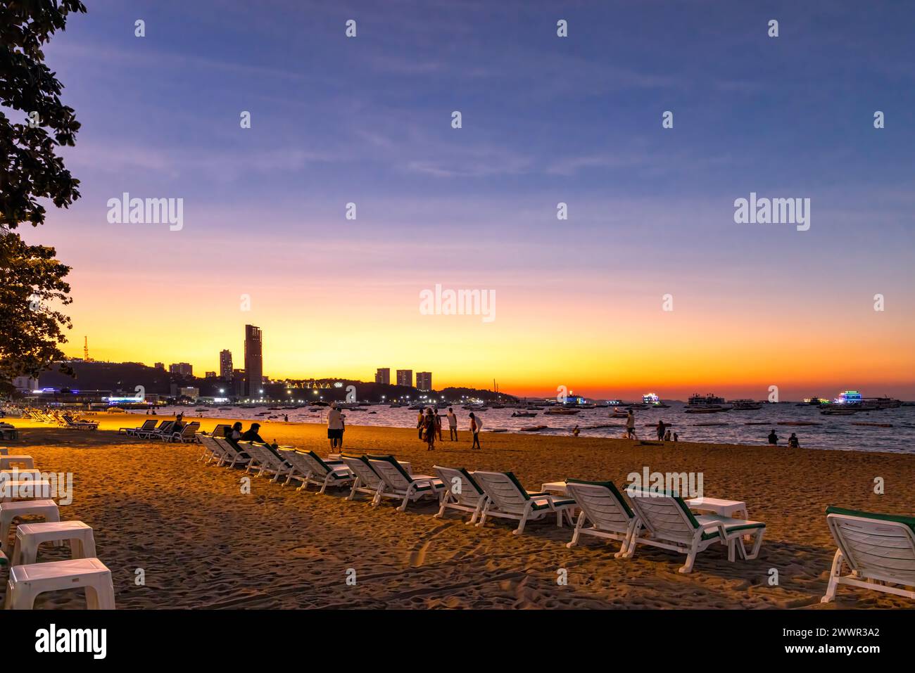 Pattaya Strandlandschaft mit Sand, Liegestühlen, Gebäuden, Menschen und Skyline bei Sonnenuntergang, Thailand Stockfoto