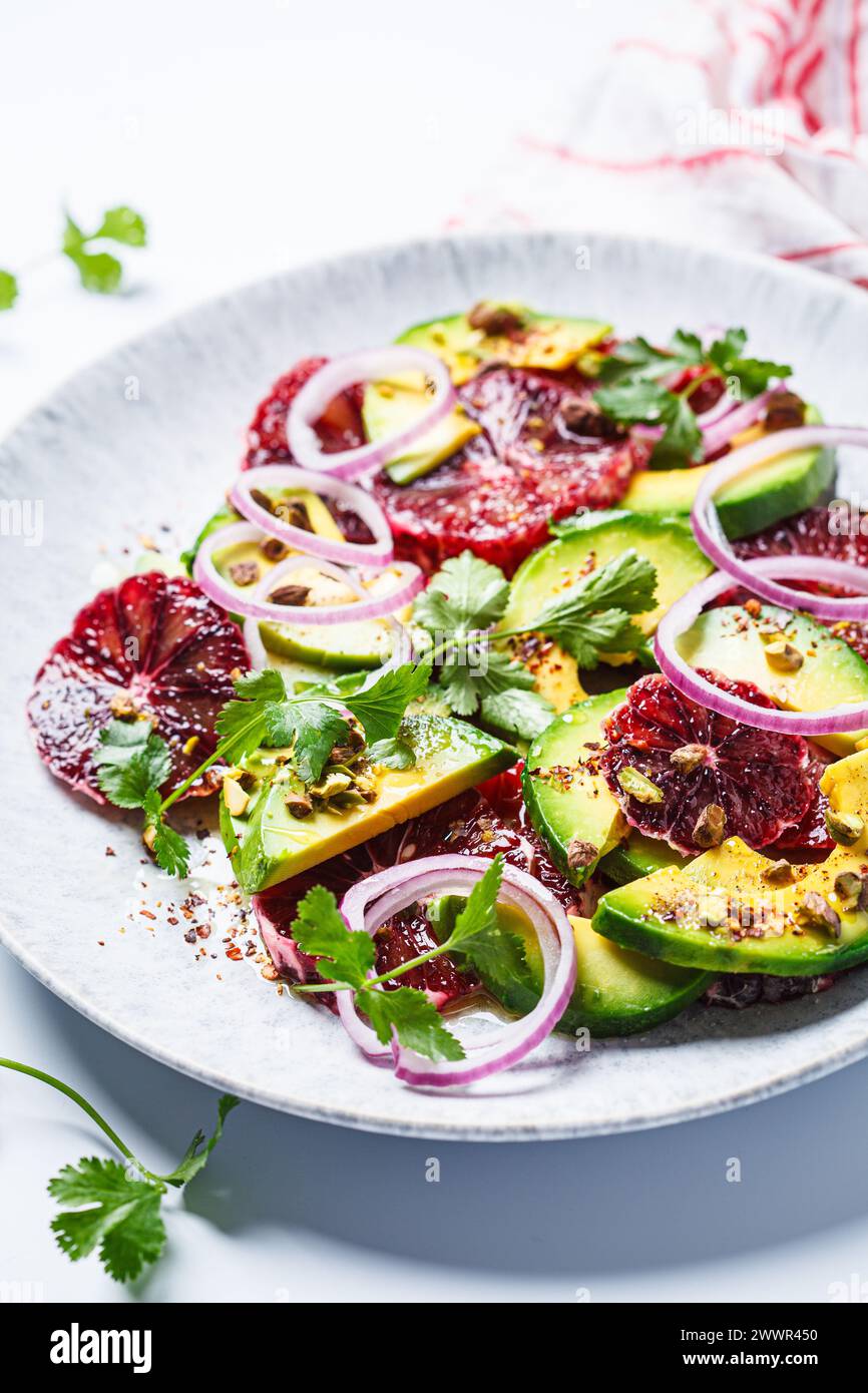 Blutorangen-Salat mit Avocado, Pistazien und roten Zwiebeln, weißer Hintergrund, Nahaufnahme. Stockfoto