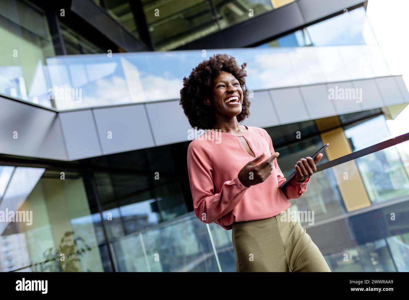 Eine Frau steht selbstbewusst vor einem modernen Gebäude, mit Tablet in der Hand, und blickt in die Zukunft. Stockfoto