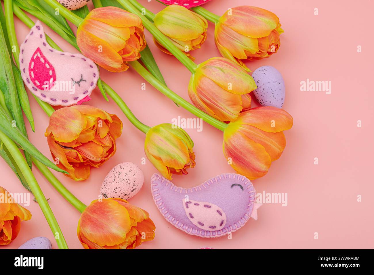 Sanfte Osterkomposition mit Tulpenblüten und handgefertigten Filzvögeln. Traditionelle dekorative Elemente, Grußkarte. Flach, rosafarbener Hintergrund, oben Stockfoto