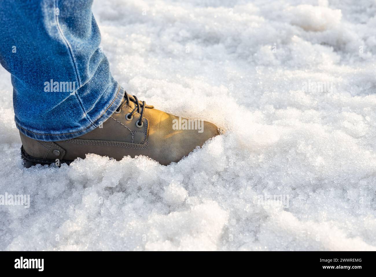 Ein Mann in Stiefeln geht durch geschmolzenen Schnee. Der Mensch läuft auf losem Schnee. Matschiger Schnee. Hochwertige Fotos Stockfoto