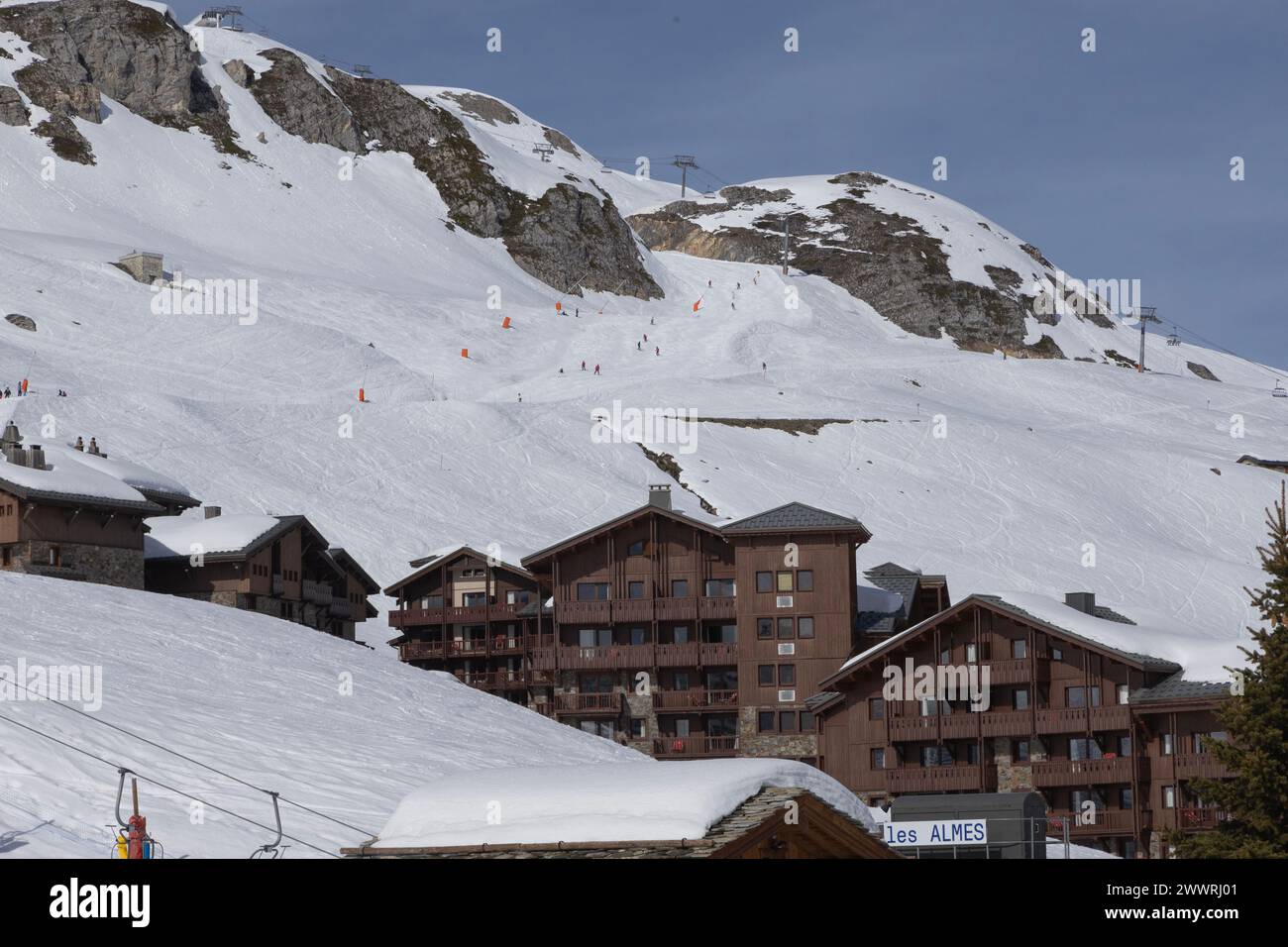 Skifahrer, die die Rote Piste „Bleuets“ in Tignes, Frankreich, über den Chalets des Almes-Viertels in diesem eigens erbauten, hochgelegenen Skigebiet hinunterfahren. Stockfoto