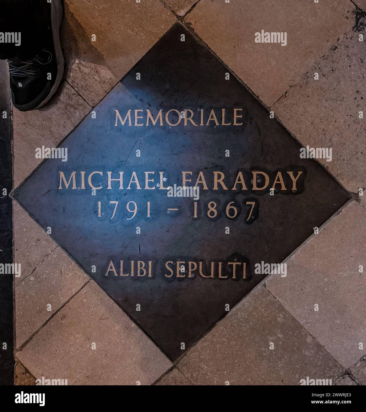 Gedenktafel von Michael Faraday, 1791-1867, mit der Aufschrift „Alibi Sepulti“ auf einem Steinboden, mit einer Teilansicht des Schuhs einer Person am Rand. Stockfoto