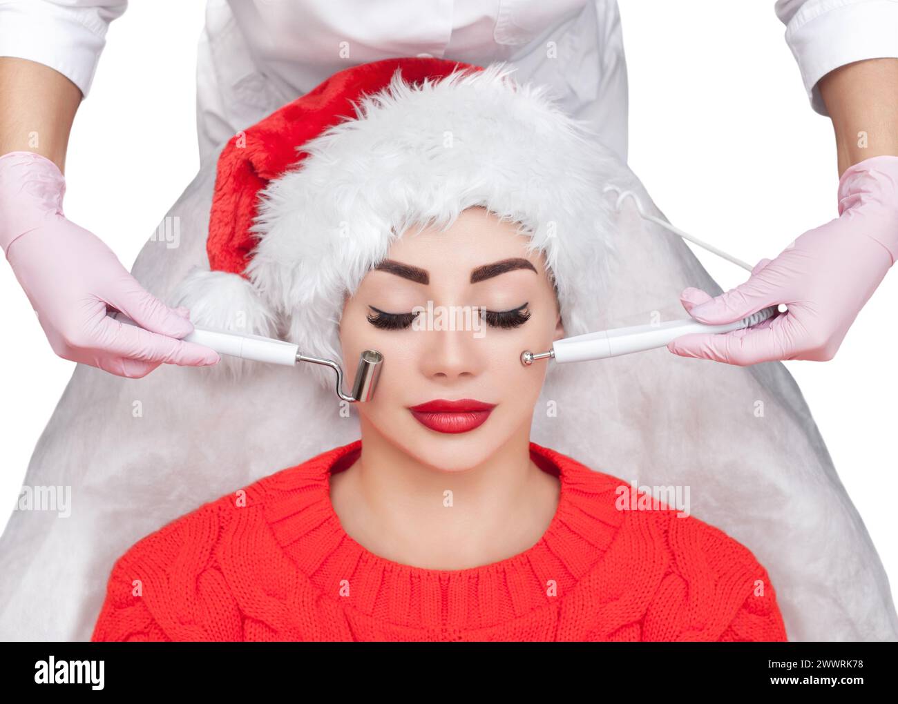 Der Kosmetiker macht das Verfahren der Mikrostromtherapie einer schönen, jungen Frau mit Santa Claus Hut in einem Schönheitssalon. Silvester und Cosmet Stockfoto