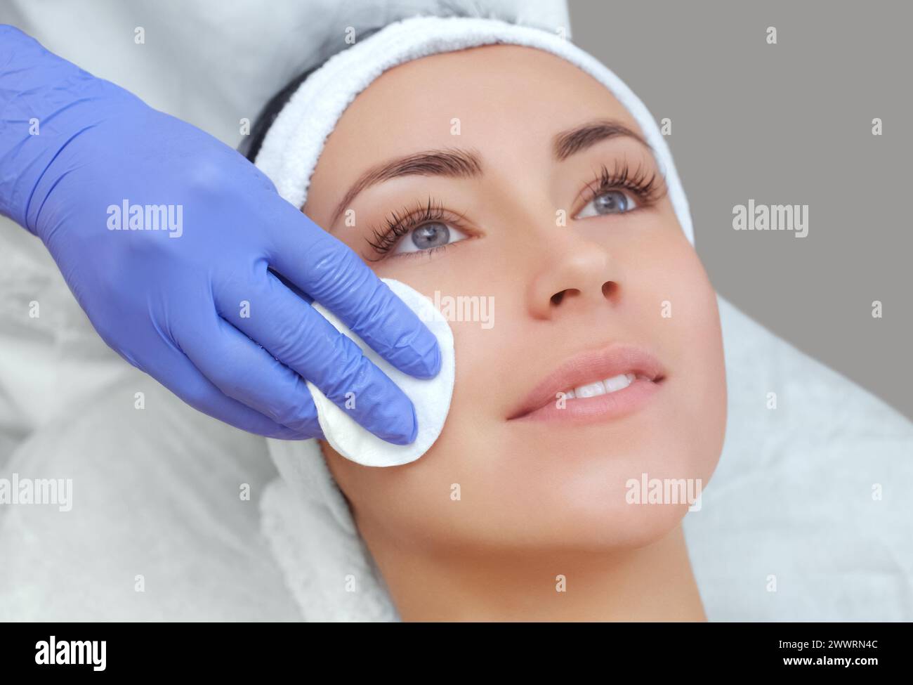 Die Kosmetikerin reinigt mit einem Tonikum die Gesichtshaut einer schönen, jungen Frau in einem Schönheitssalon. Stockfoto