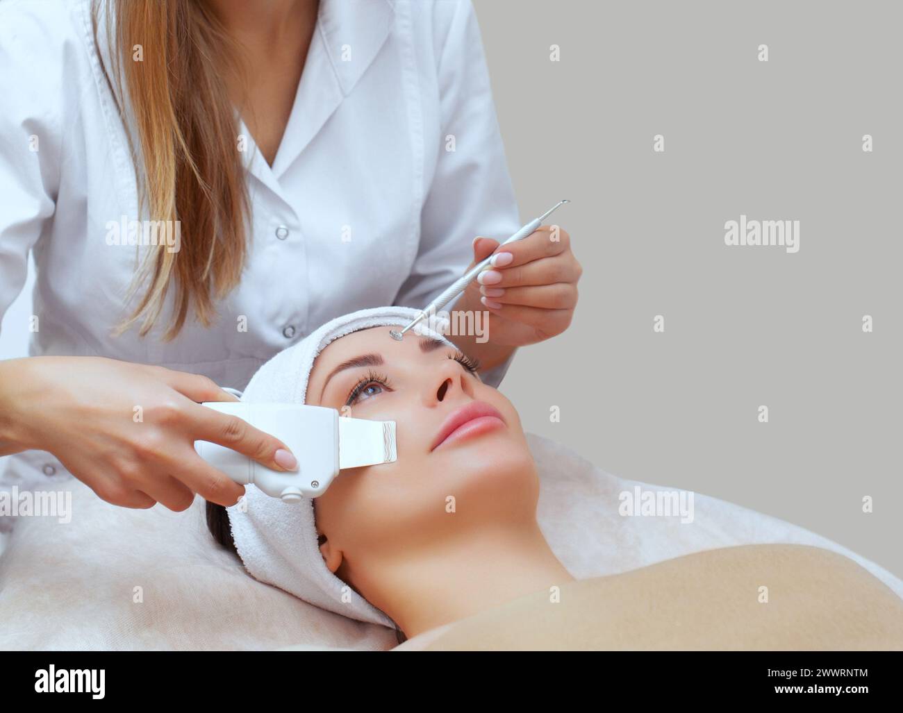 Der Arzt-Kosmetologe macht das Gerät zu einem Verfahren der Ultraschallreinigung der Gesichtshaut einer schönen, jungen Frau in einem Schönheitssalon. Kosmos Stockfoto