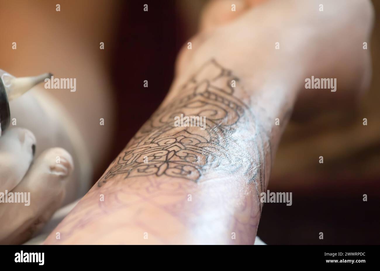 Tattoo Master Schutzhandschuhe machen ein Tattoo in schwarzer Tinte auf der Hand des Mädchens. Stockfoto