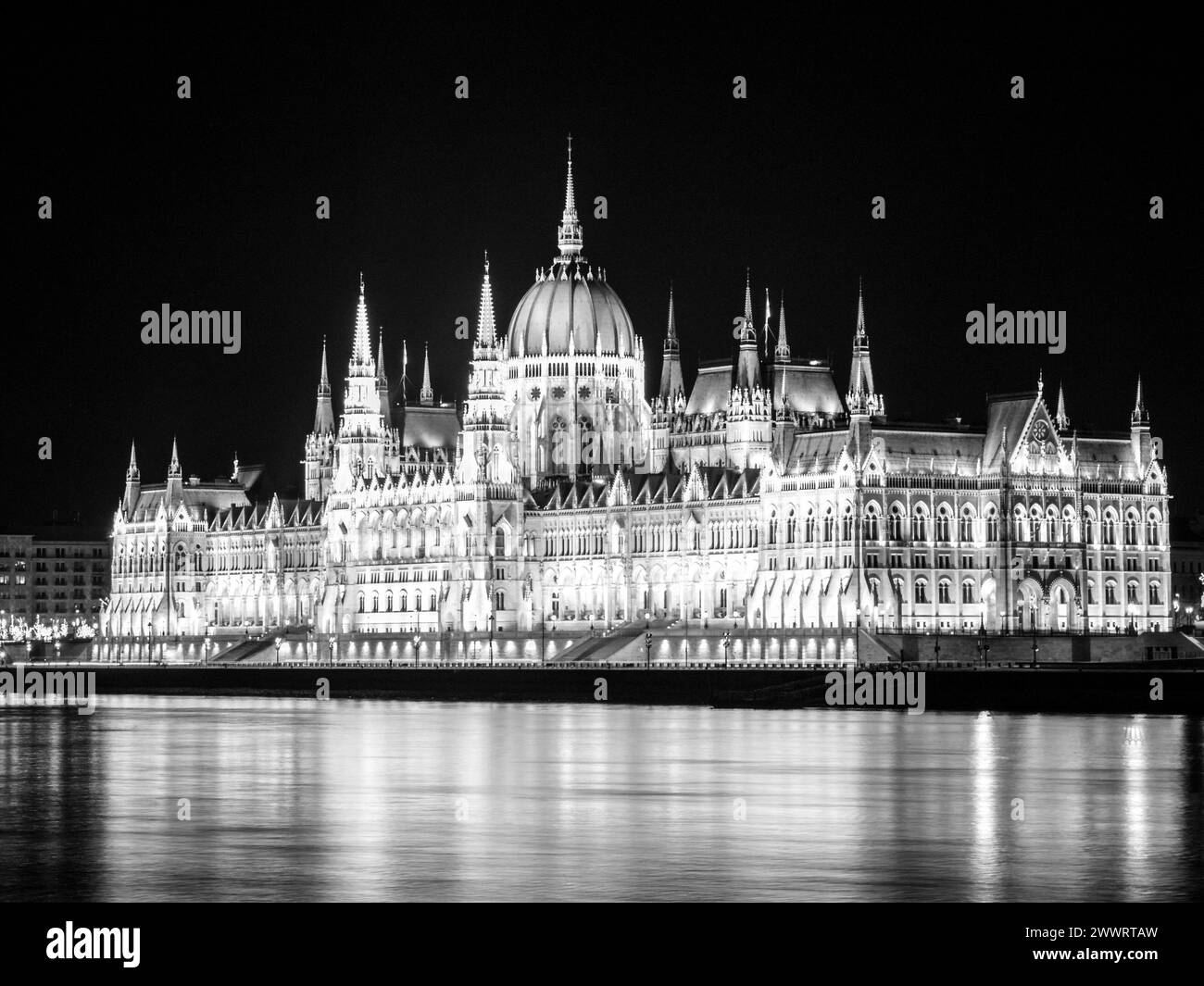 Nachtansicht des beleuchteten historischen Gebäudes des ungarischen Parlaments, aka Orszaghaz, mit typischer symmetrischer Architektur und zentraler Kuppel auf dem Donauufer in Budapest, Ungarn, Europa. Es ist ein bemerkenswertes Wahrzeichen und Sitz der Nationalversammlung von Ungarn. Schwarzweiß-Bild. Stockfoto
