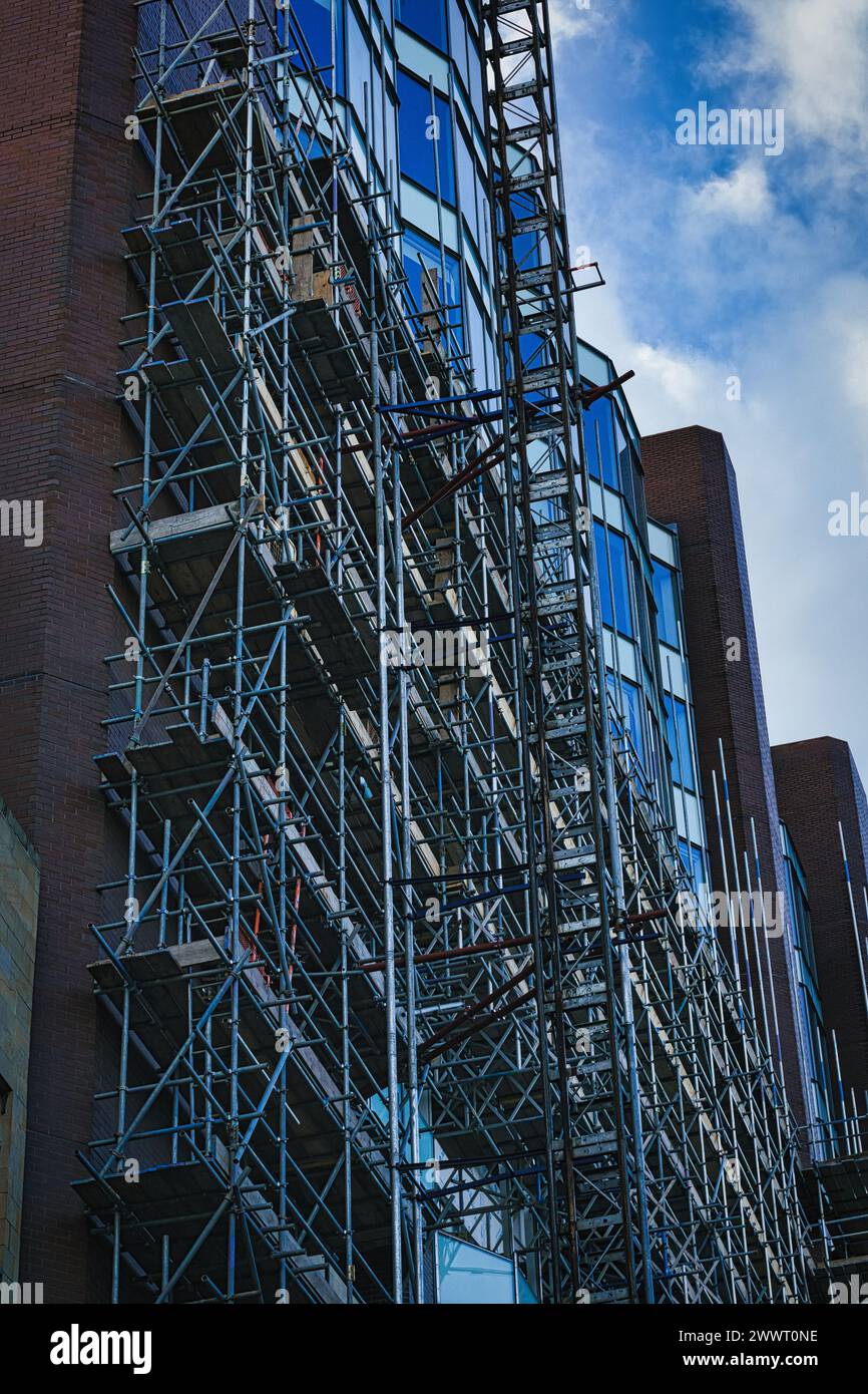 Komplexe Gerüstkonstruktion an der Seite eines modernen Gebäudes mit Glasfassade vor blauem Himmel in Leeds, Großbritannien. Stockfoto