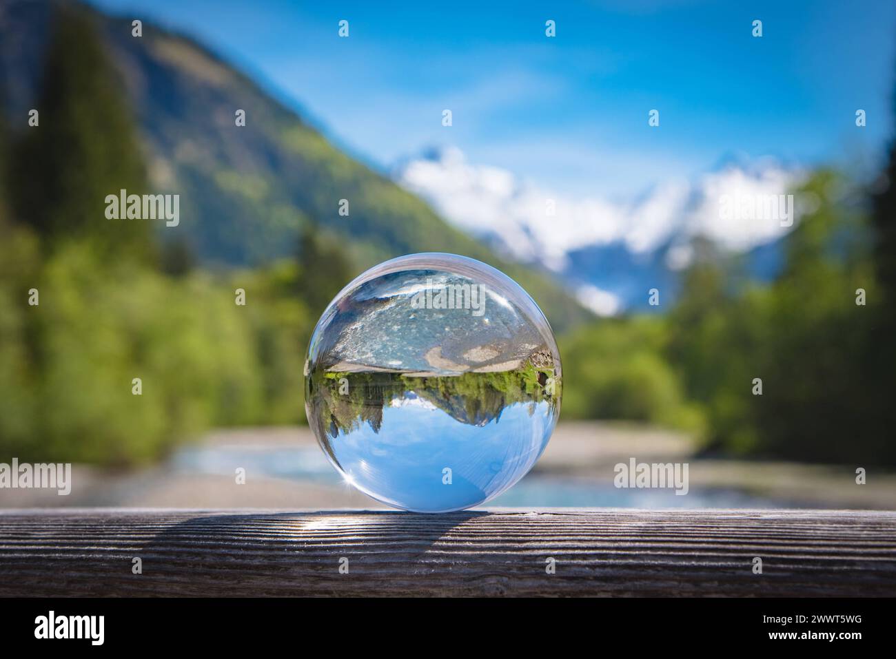 Wildbach in den Bergen mit Alpenpanorama im Hintergrund spiegelt sich in einer Glaskugel. Schmelzwasser führende Wildbäche in den Alpen wie zum Beispiel die Breitachklamm sind eine interessante Sehenswürdigkeit und beliebtes Ausflugsziel - auch an Tagen mit schlechtem Wetter. Es gibt verschiedene Wandertouren entlang solcher Gewässer die dann teils über Stege entlang von Stromschnellen und kleinen Wasserfällen führen. Raum Oberstdorf Bayern Deutschland *** Bergbach mit Panoramablick auf die Alpen im Hintergrund reflektiert in einer Glaskugel Ströme, die Schmelzwasser in die Berge tragen Stockfoto