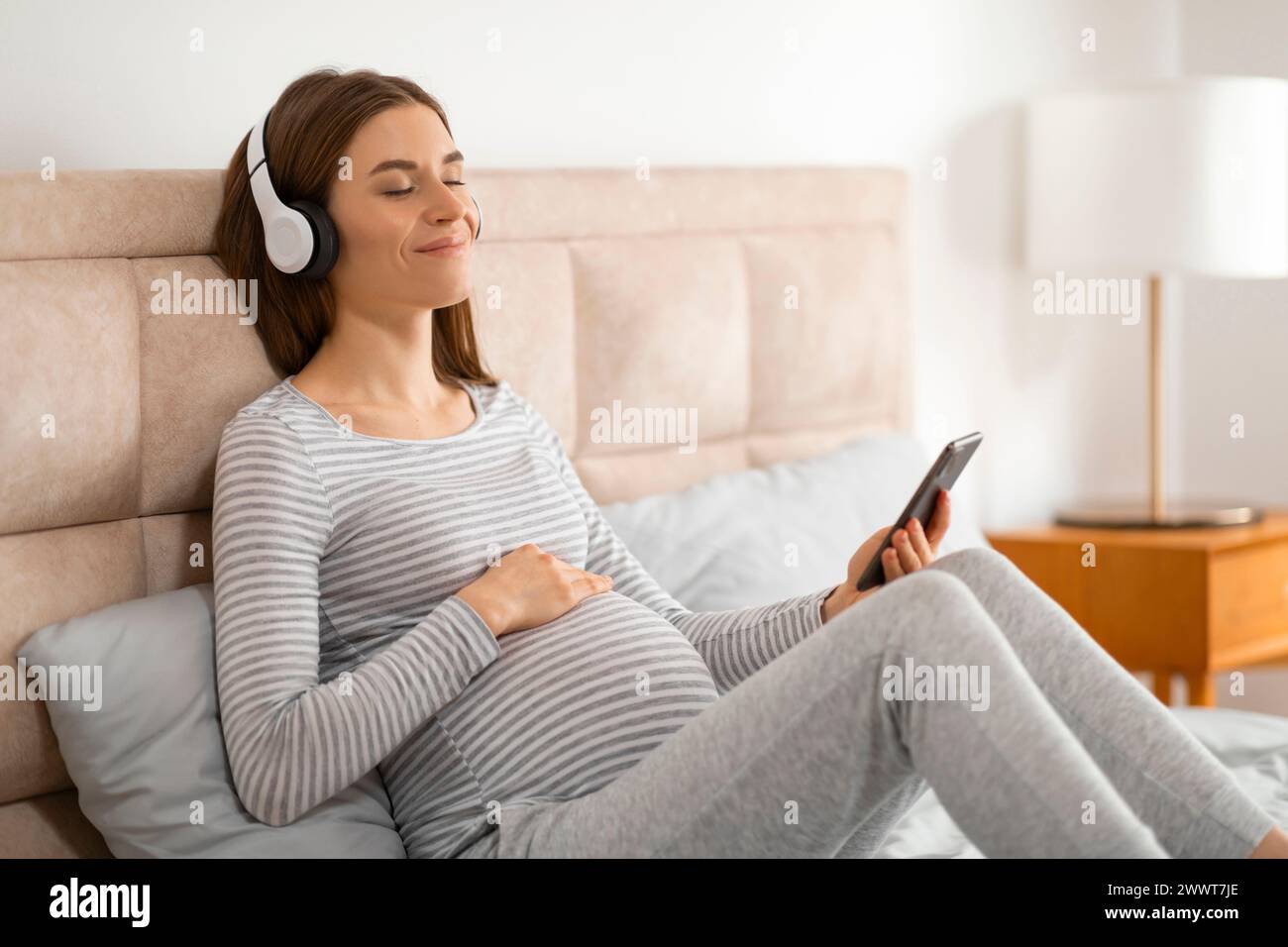 Ich erwarte die Mutter, die sich mit Kopfhörern und Telefon entspannt Stockfoto
