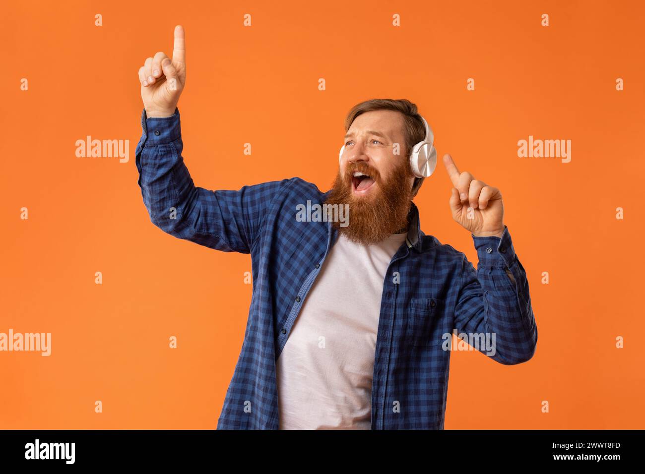 Porträt eines lustigen Kerls, der Musik in Kopfhörern hört, im Studio Stockfoto